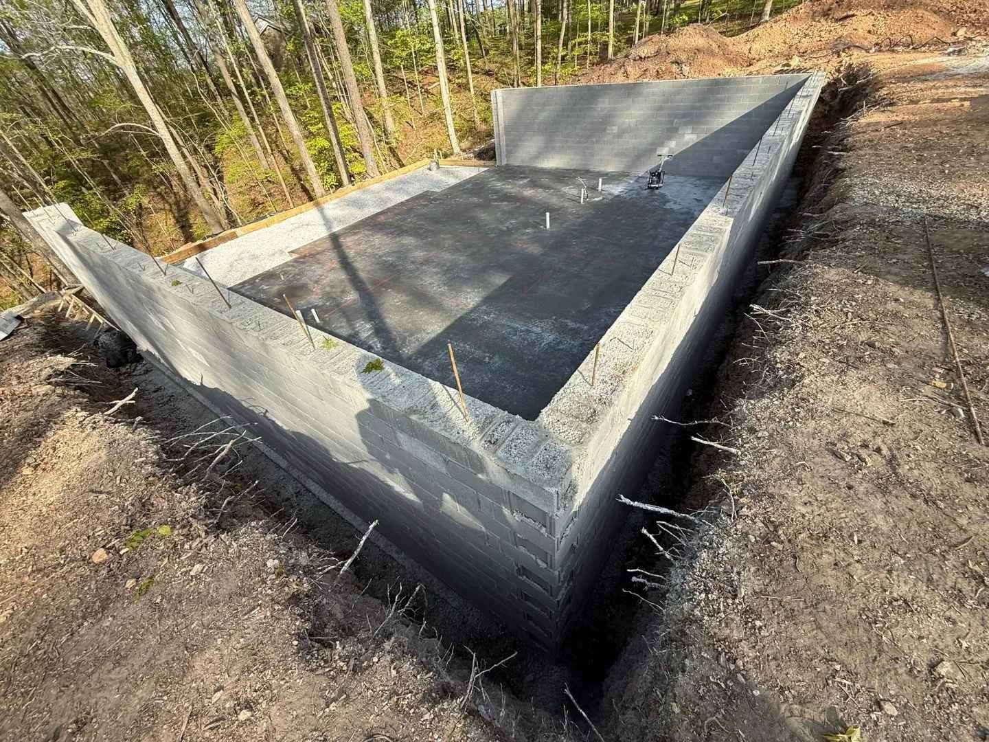 Concrete basement foundation with block stem walls and exterior waterproofing on a sloped wooded lot
