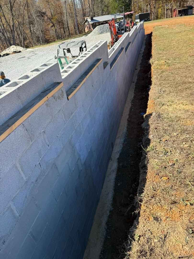 A block foundation wall with dark gray coating and a trench dug along the base.
