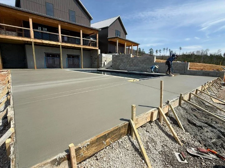 Freshly poured concrete pool deck installation in McMinnville, TN, with smooth finish, forming boards still in place, and block retaining walls surrounding the pool area.
