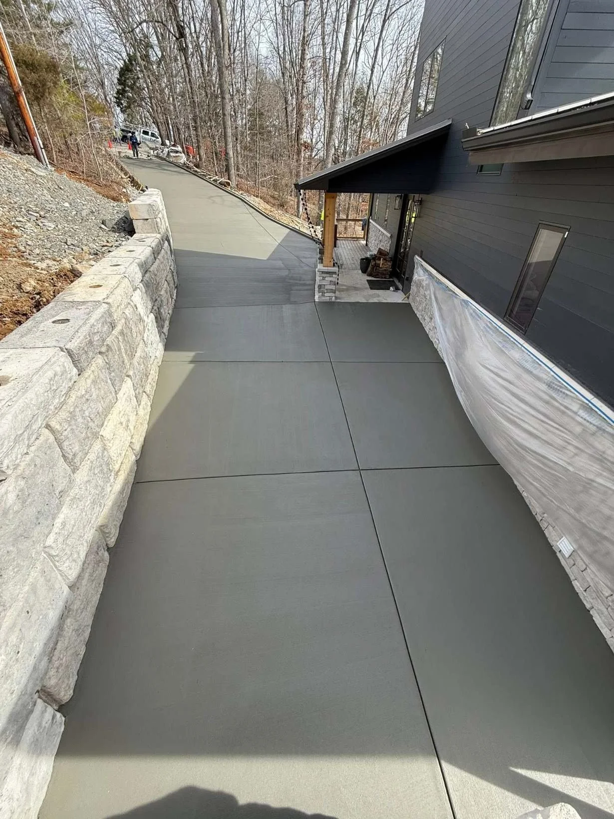 Close-up of the finished driveway with curbs running along a stone wall. Clean control joints cut in and a smooth finish throughout.