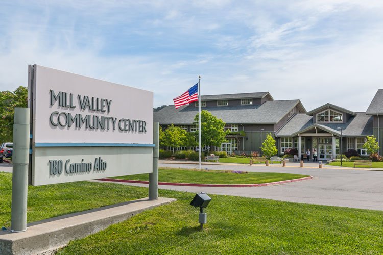 Mill Valley Community Center sign in front with a building, American flag, and trees in the background.