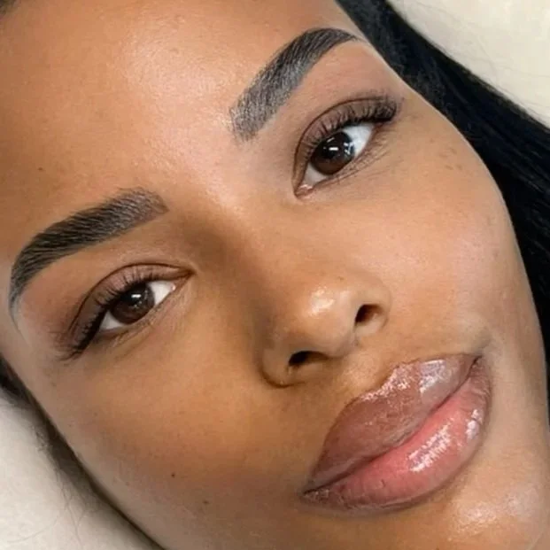 Close-up of a woman's face showing well-groomed eyebrows, brown eyes, and glossy lips.