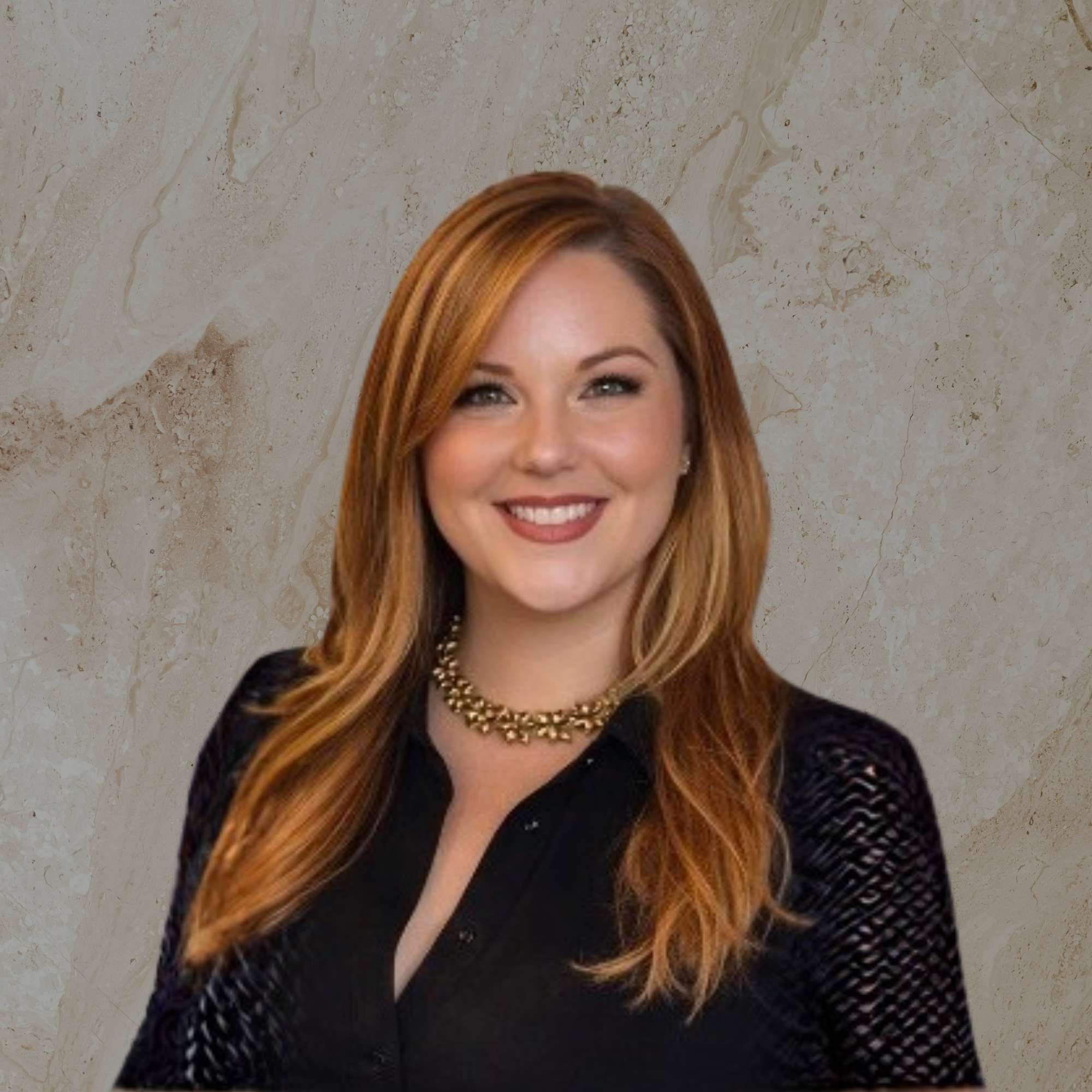 Close-up of a woman smiling with wavy auburn hair, wearing a black dress with mesh sleeves and a gold necklace, against a beige marble background.