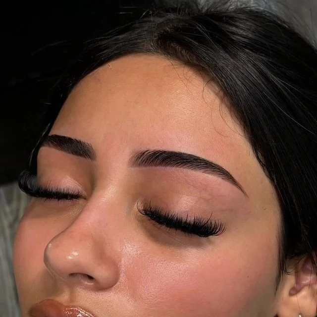 Close-up of a woman's face with makeup, showing her closed eyes, well-groomed eyebrows, and long false eyelashes.