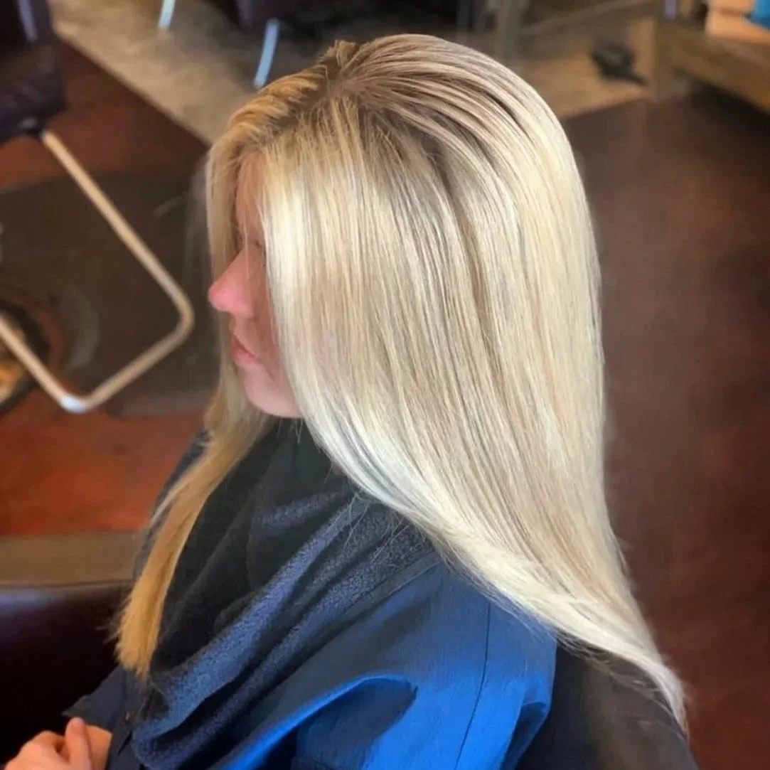 Side view of a woman with long, straight, blonde hair sitting in a salon chair.