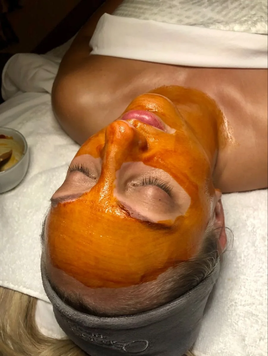A woman lying on a spa bed with an orange facial mask covering her face.
