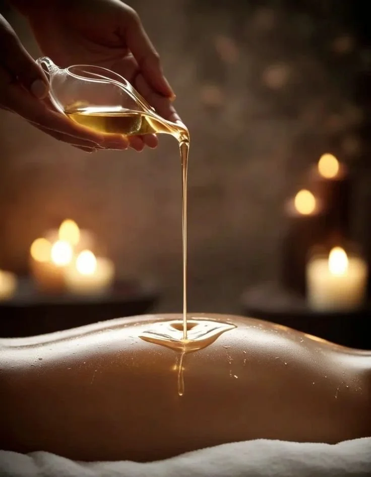 Person pouring warm massage oil onto their back during a massage in a spa setting with candlelight in the background.
