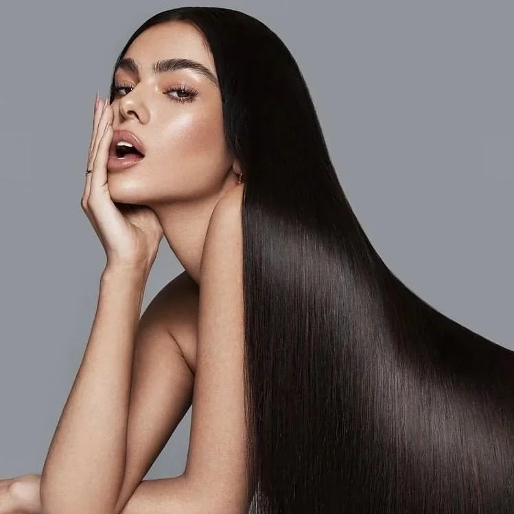 A woman with long, straight, dark hair poses against a gray background.