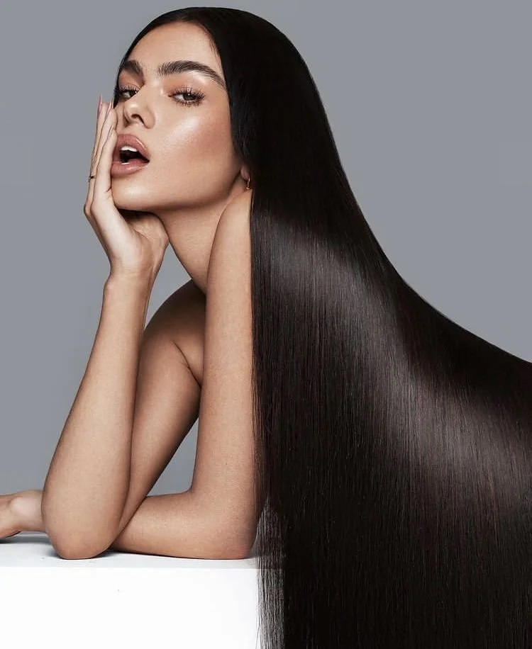 Professional portrait of a woman with long, straight, dark hair posing against a gray background.