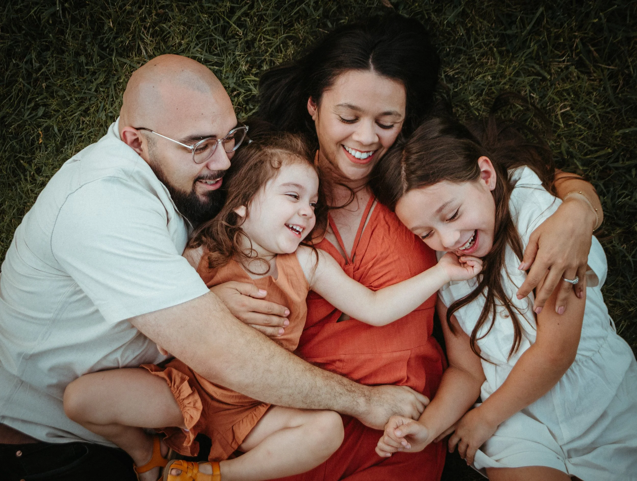 A family of five lying on grass, smiling and hugging each other.