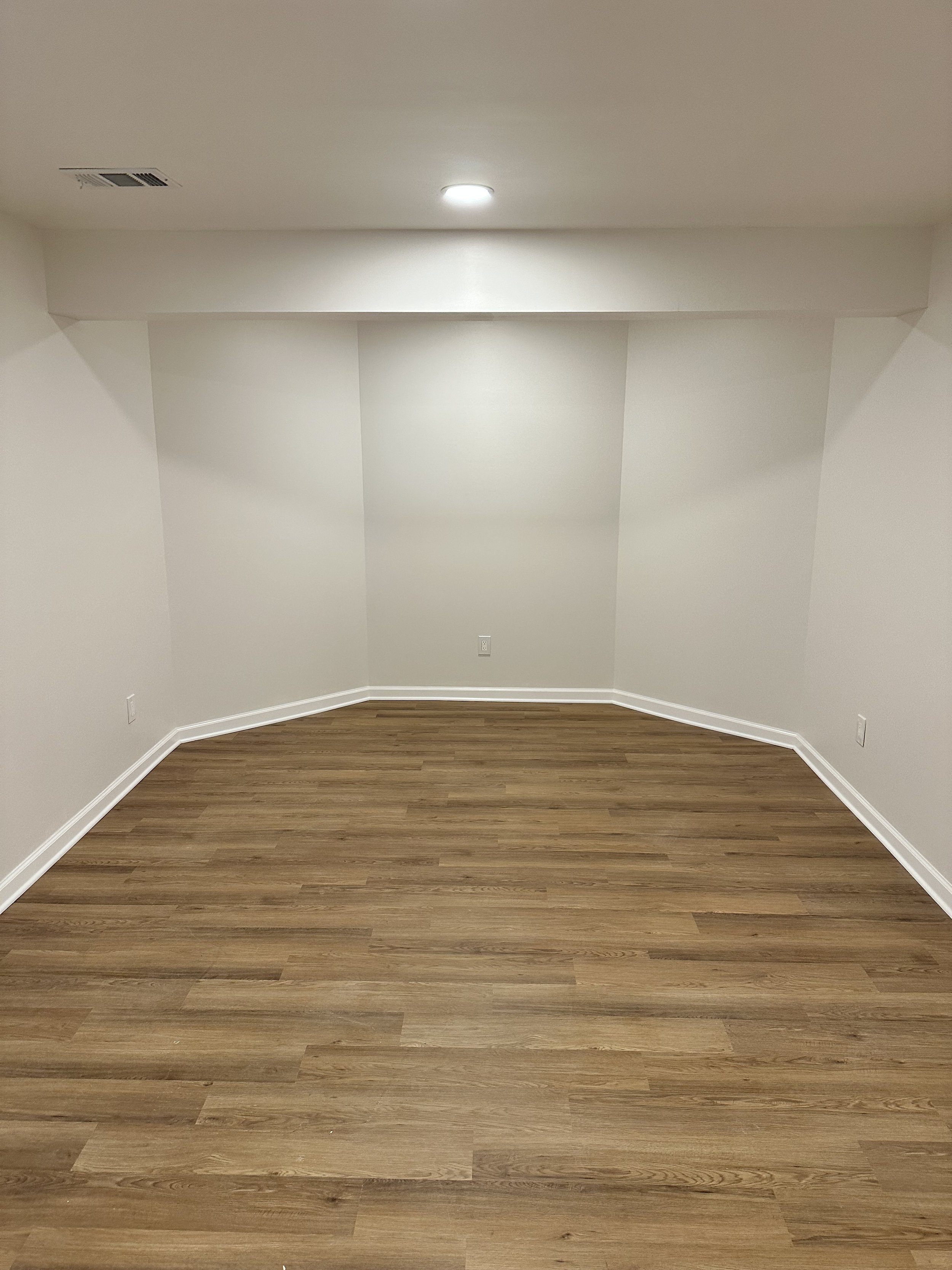 Empty room with plain white walls, medium-toned wood flooring, and ceiling lights.