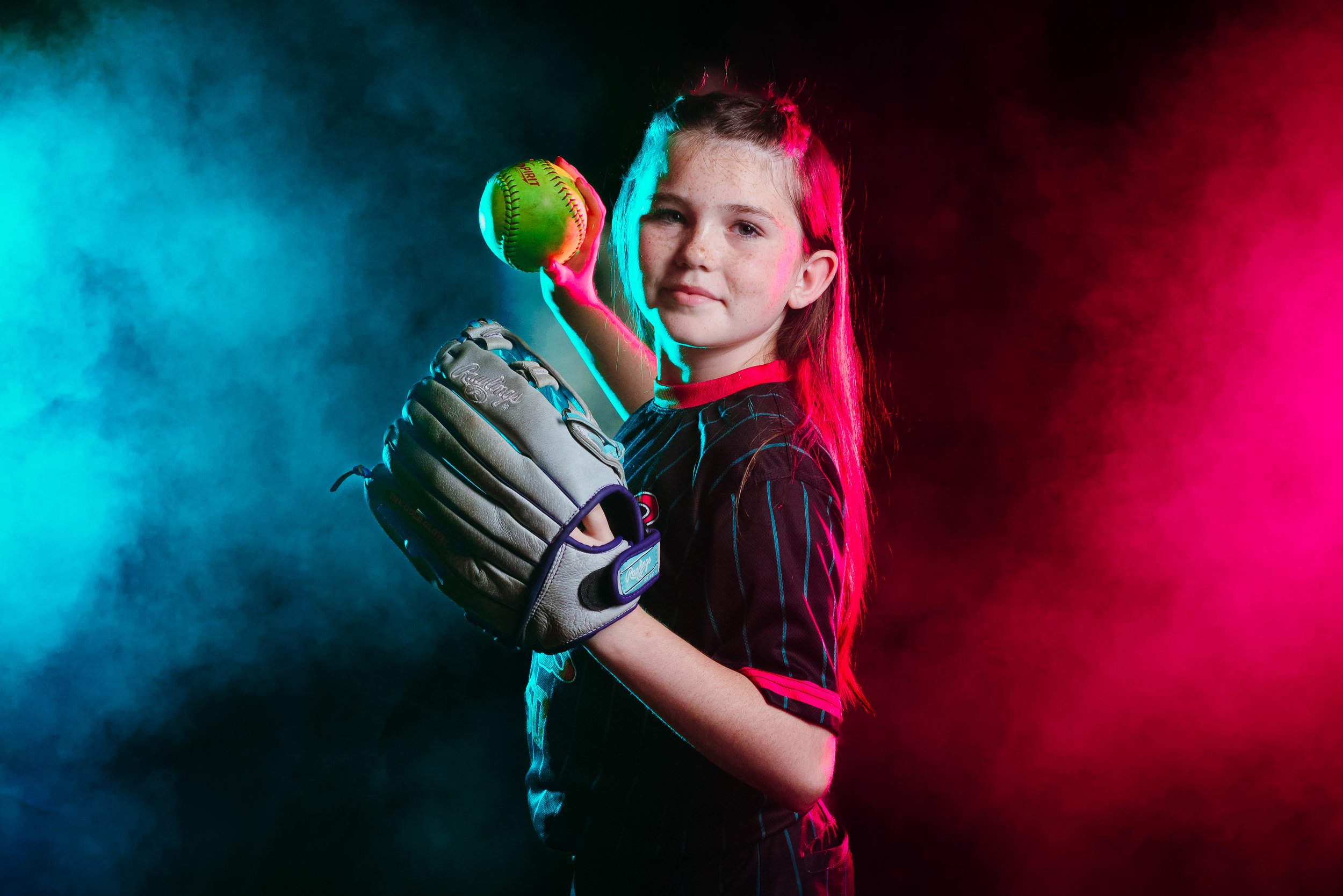Female softball player posing with dramatic lighting and team uniform