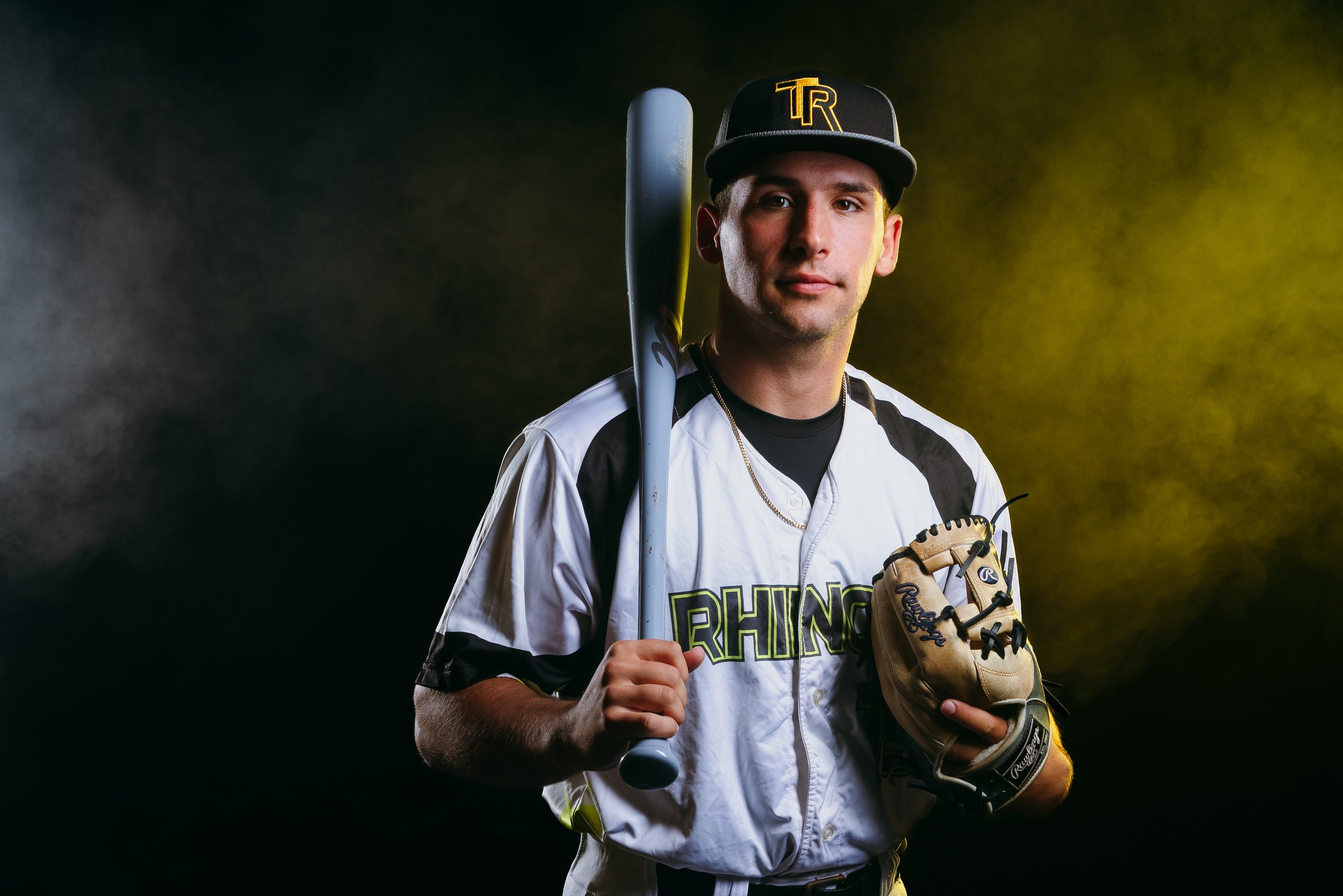 Baseball player from the Texarkana Rhinos of the Mid-America League posing with dramatic gel lighting and smoke effects during a stylized sports portrait session