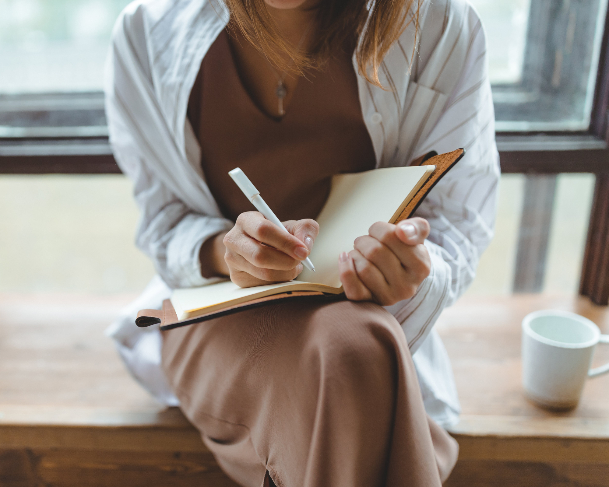 Close-up of a woman writing in a notebook with a pen, seated at a table.