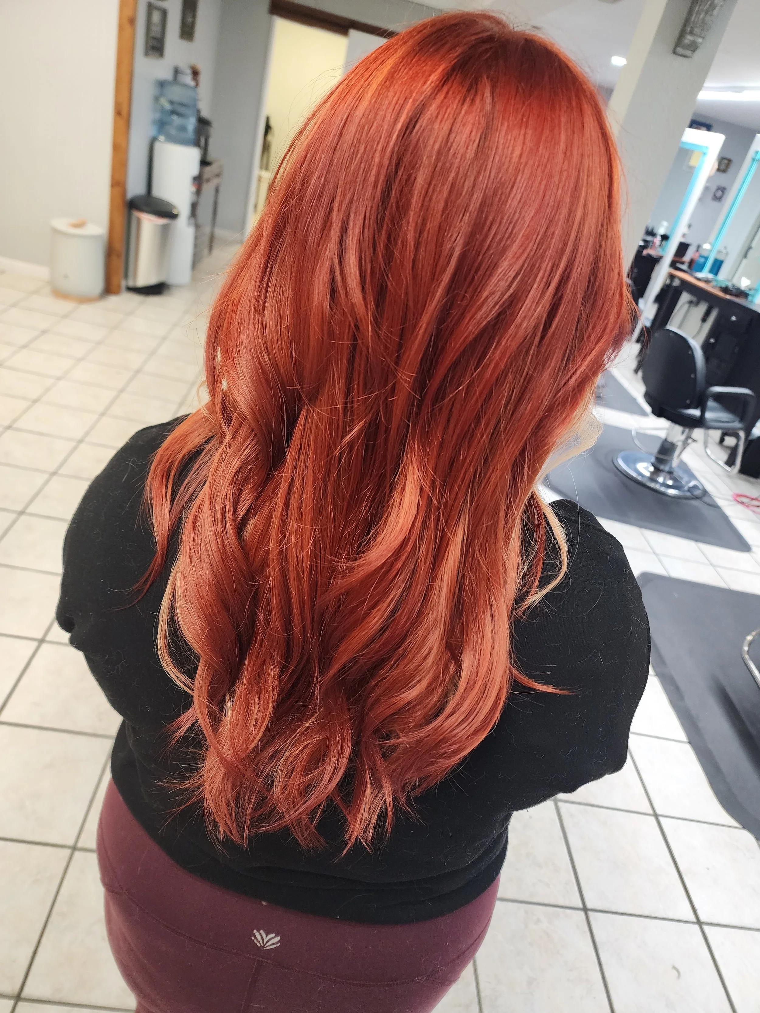 Back of woman with long, wavy, red hair in a hair salon.