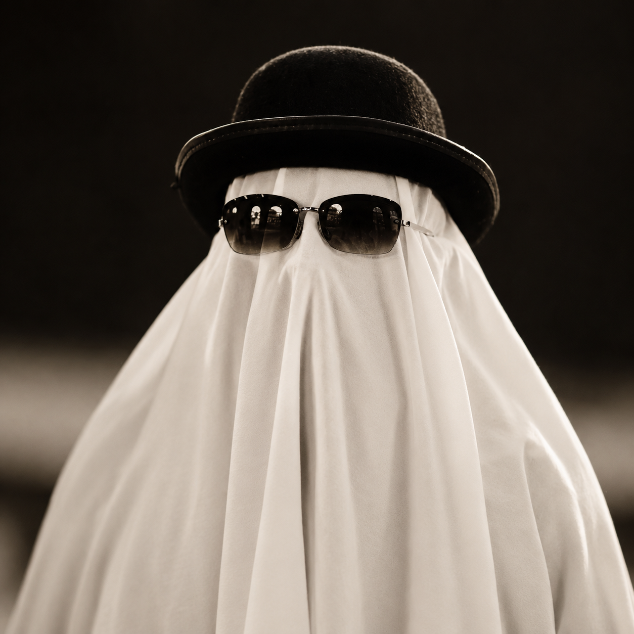 A ghost costume made from a white sheet with eye holes, accessorized with sunglasses and a black top hat.