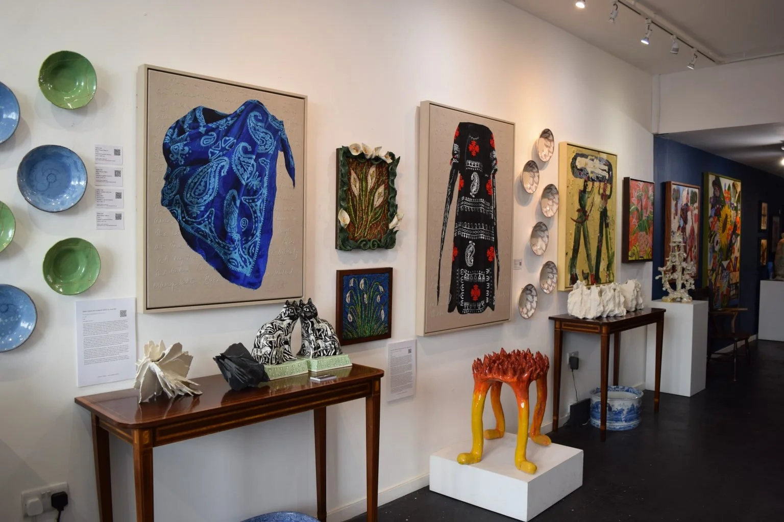 Blue storefront of Alveston Fine Arts with large glass windows displaying artwork inside, and a blue awning with white text, including website URL. Outside, a small black chair is placed to the left of the entrance.