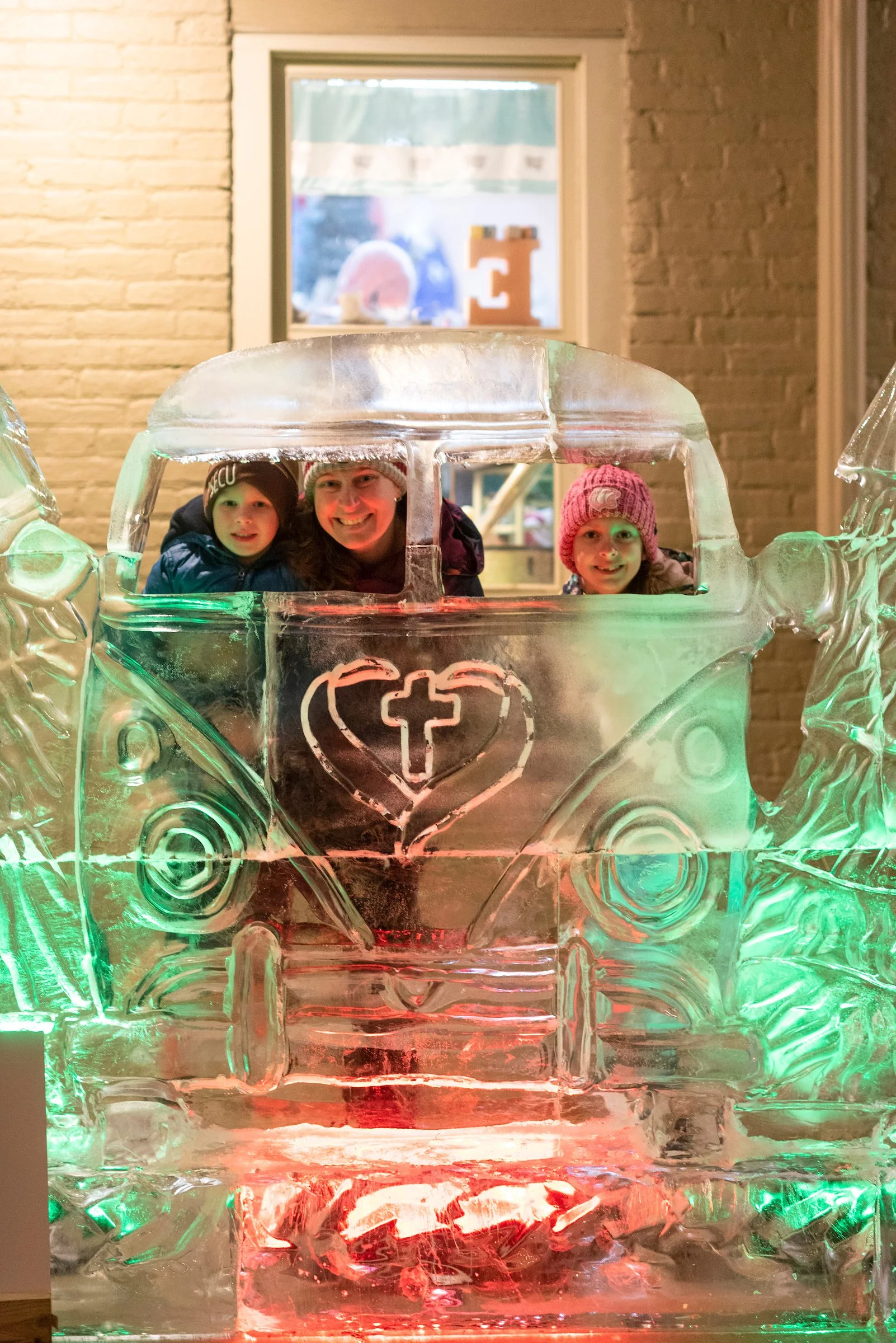 Three children and a woman inside an ice sculpture of a truck, with a cross and heart carved on the front, seen through the clear ice.