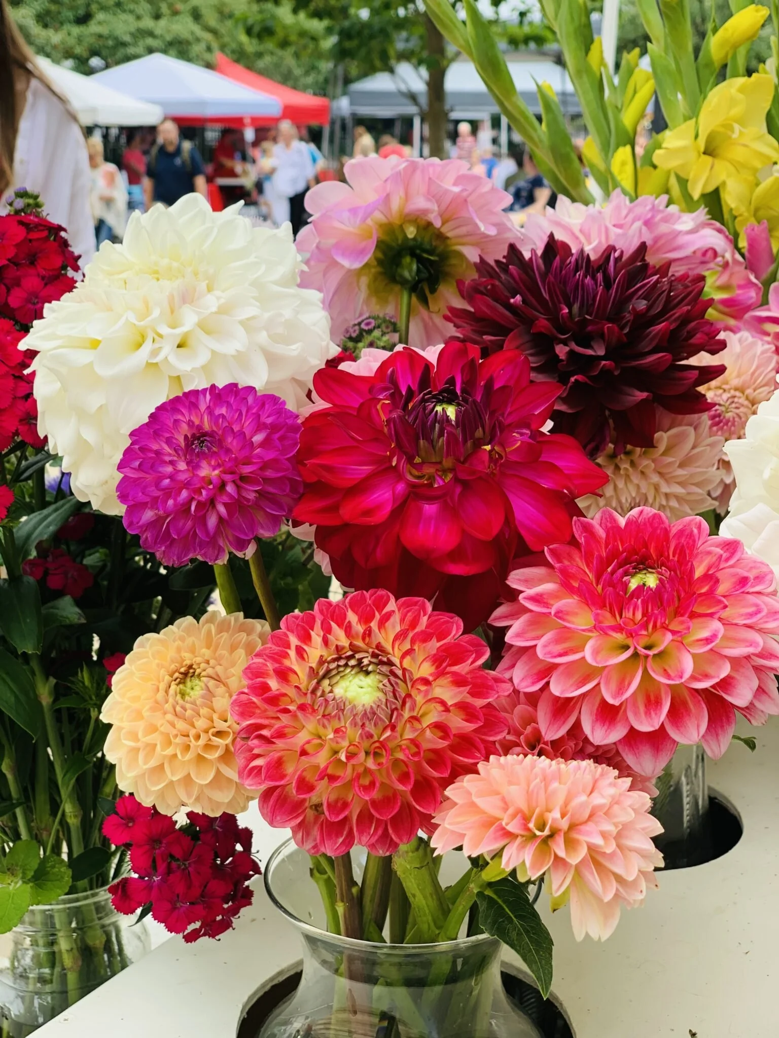 A colorful bouquet of dahlias in a clear glass vase at a flower market.