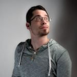 A young man with glasses and a gray hoodie looking to the side