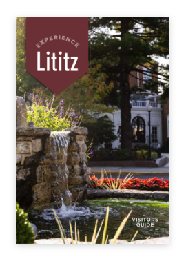 Cover of a visitors guide with a fountain, plants, and trees in front of a building, for Lititz with the title 'Experience Lititz'.