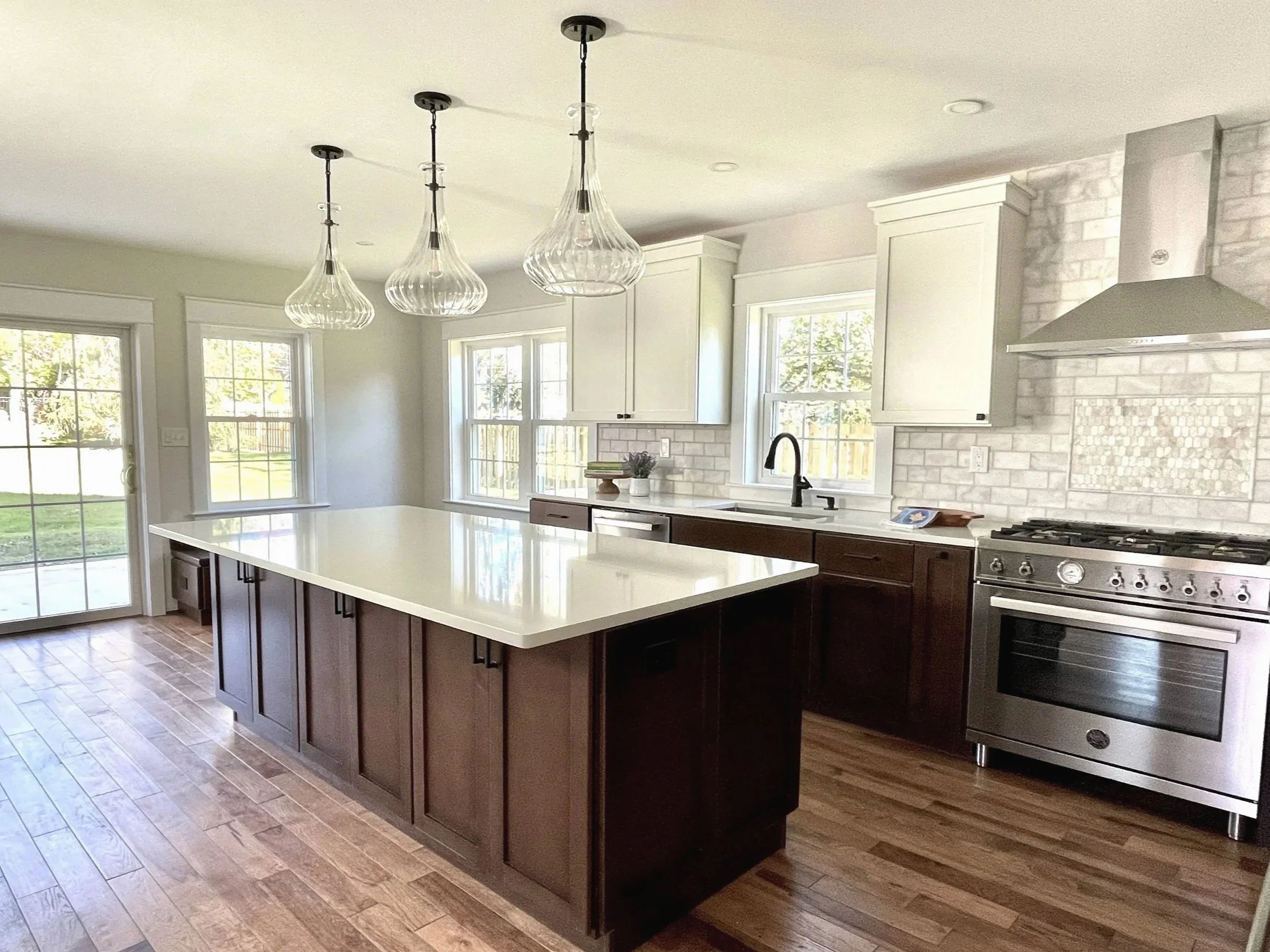 Kitchen with white upper cabinets and lower perimeter including the island in a dark walnut wood.  The design has three oversized ribbed glass mushroom shaped pendants and Bertazzoni stainless appliances, designed and photographed by Sara Trotter / C