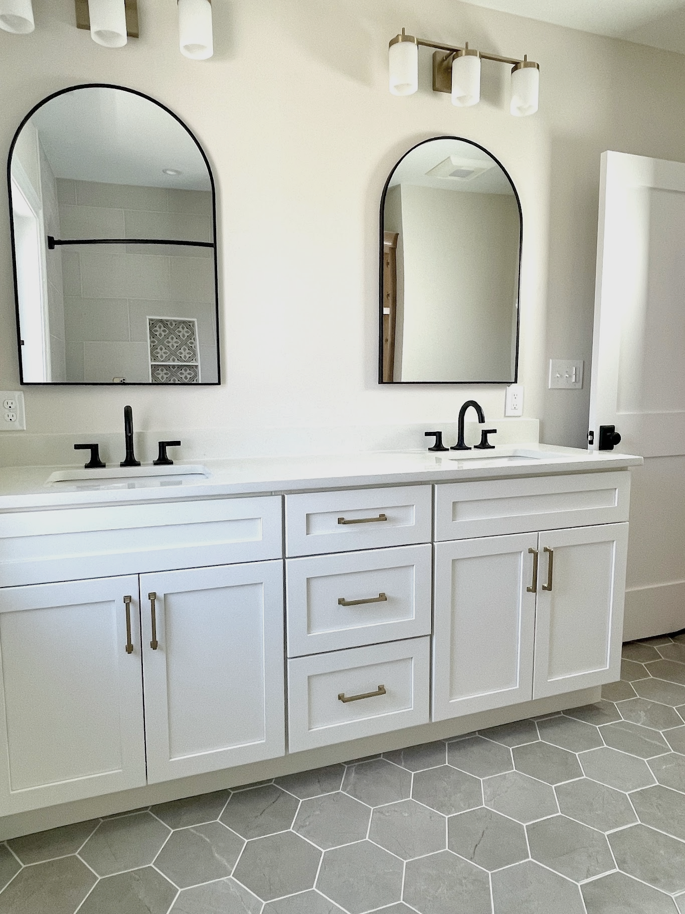 Hall bath with mixed metals of brass and matte black fixtures & hardware.  The gray hexagon floor has copper veining running throughout to tie into the hallway hardwood, designed and photographed by Sara Trotter / Chroma Maison Design.