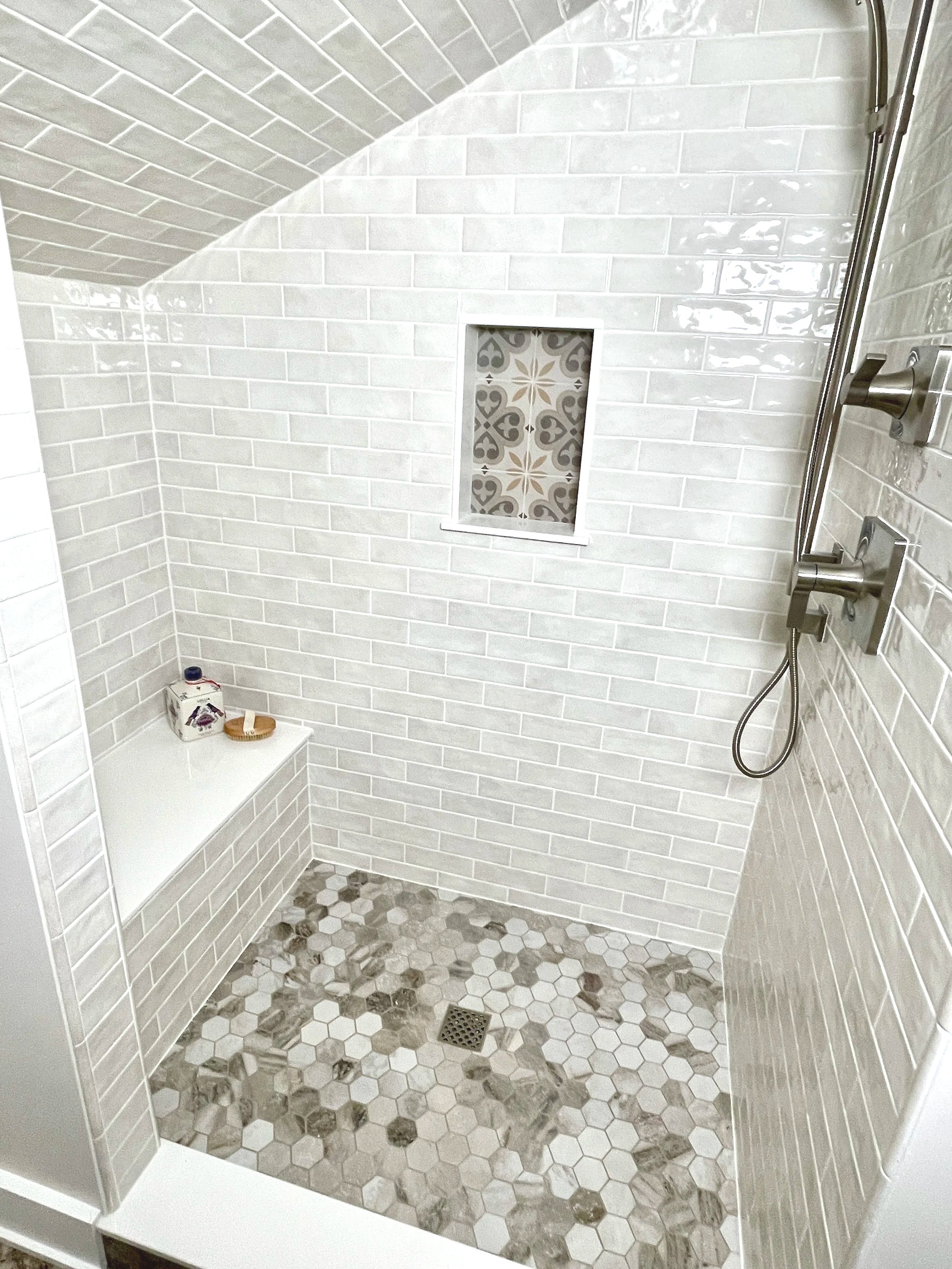 Borgo soft white faux crackle replica Victorian subway tile shower with a pattern niche box and stone hexagon shower floor.  This space was carved out of an attic area with a subway tiled shower ceiling, designed and photographed by Sara Trotter / Ch