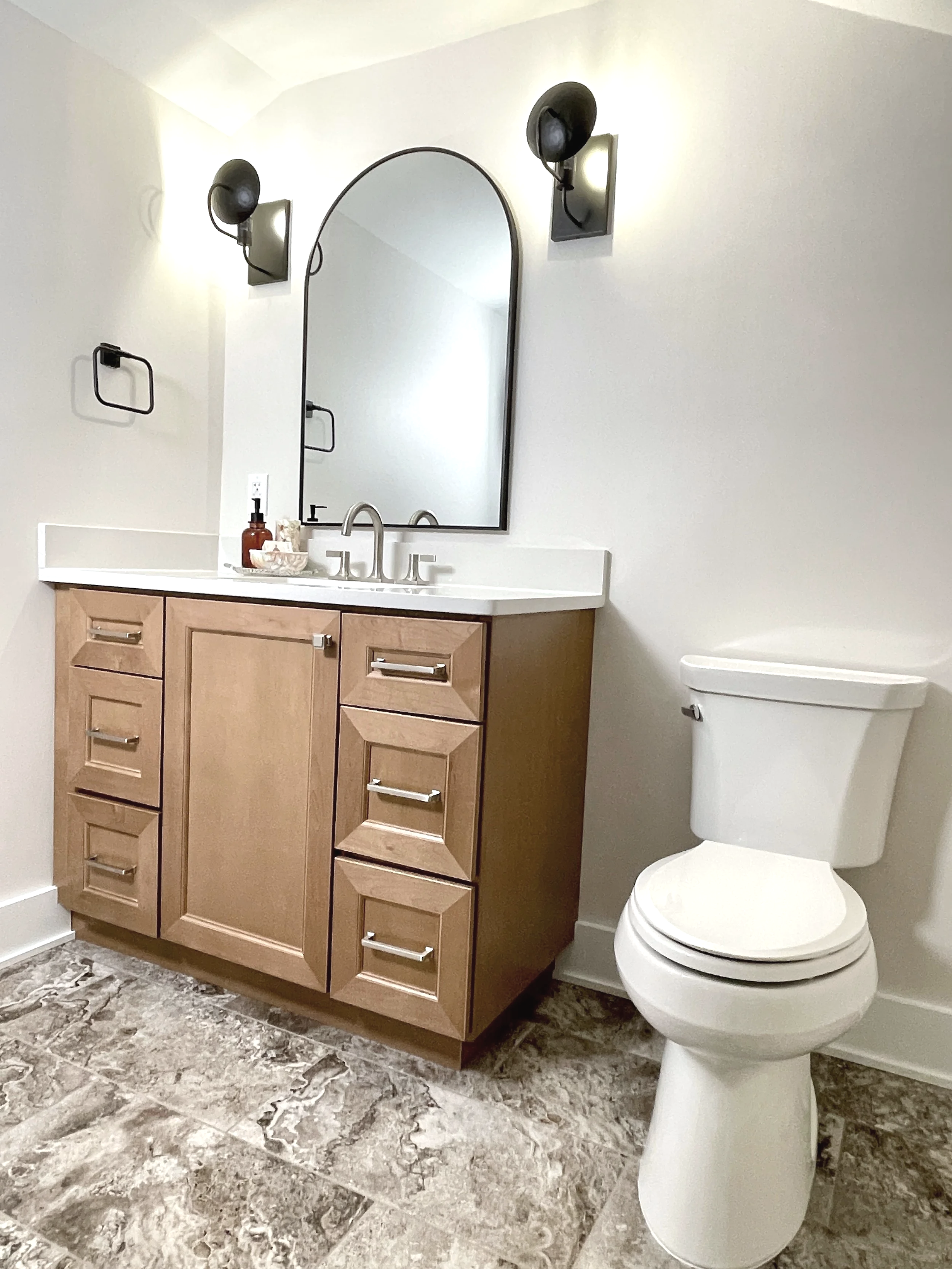 Vanity with an arched black mirror flanked on either side with Visual Comfort black iron shield sconces, designed and photographed by Sara Trotter / Chroma Maison Design.