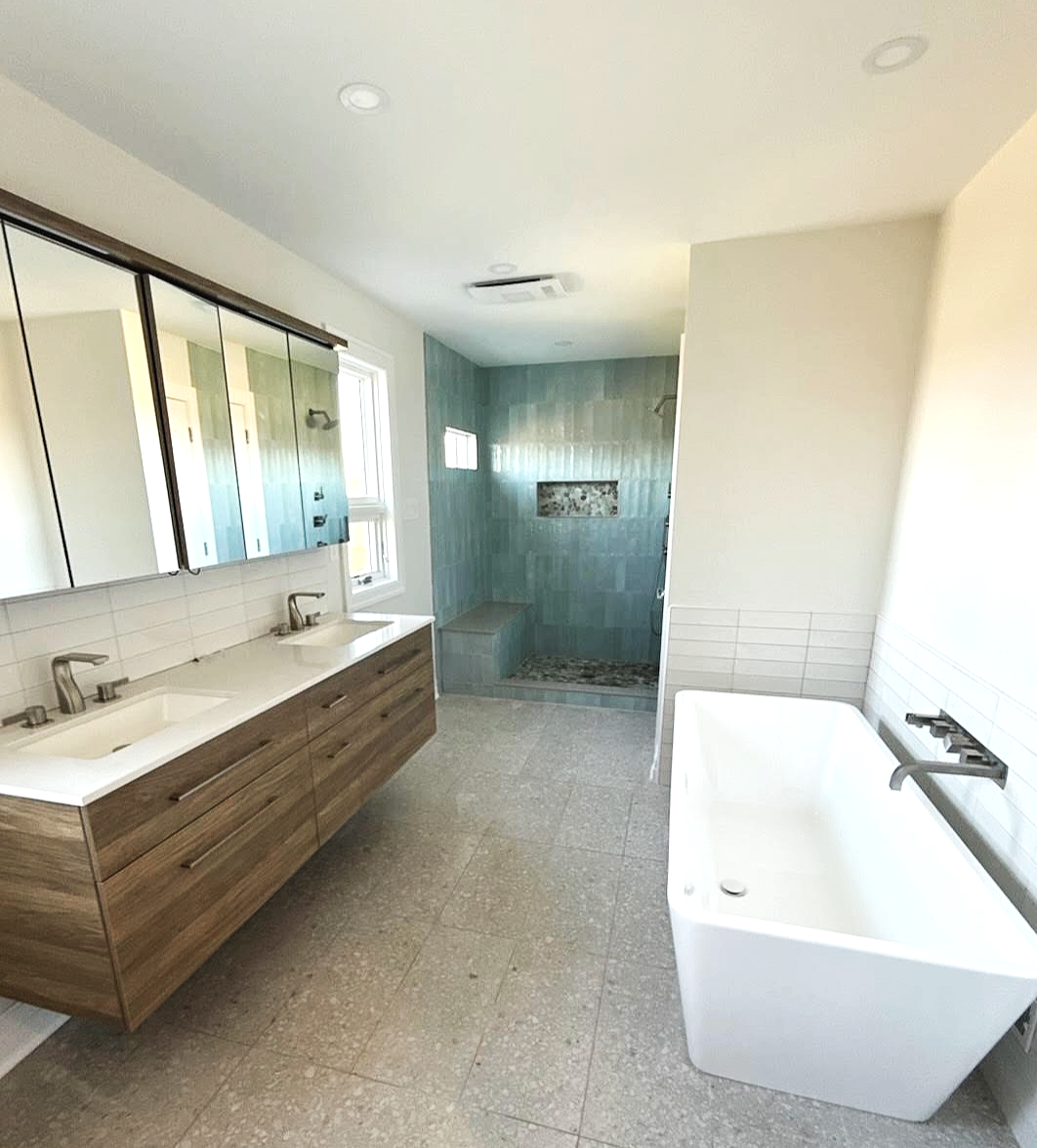 Spa bathroom featuring aqua subway tile shower walls, colorful pebbles on the shower floor, and a terrazzo main floor tile.  The full wall length Vanico medicine cabinet and floating vanity combo add more European flair, designed and photographed by 
