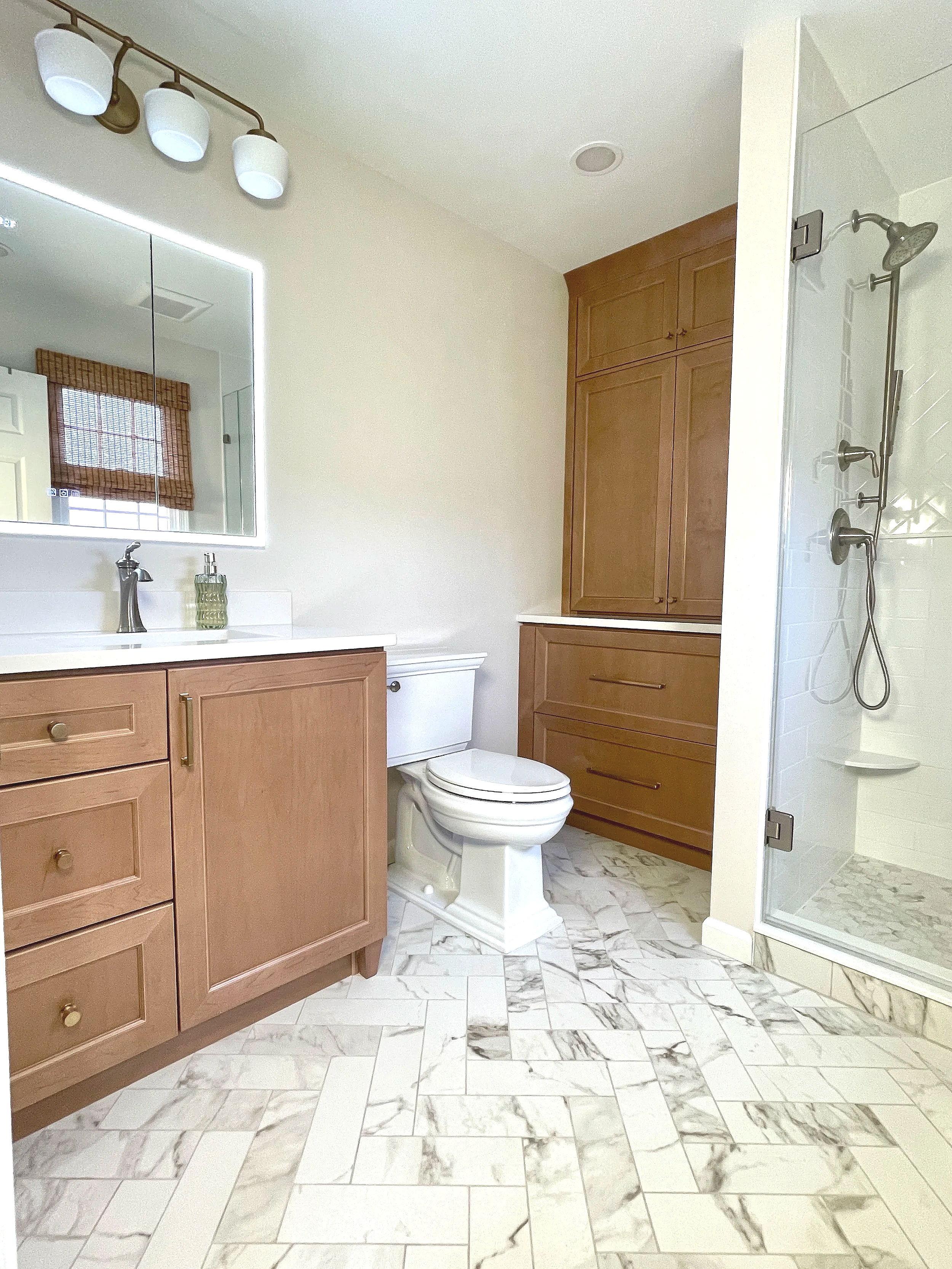 Herringbone Calacatta marble floor tile with maple Century cabinetry built-in's.  The smart mirror medicine cabinet adds a sleek modern finish, designed and photographed by Sara Trotter / Chroma Maison Design.