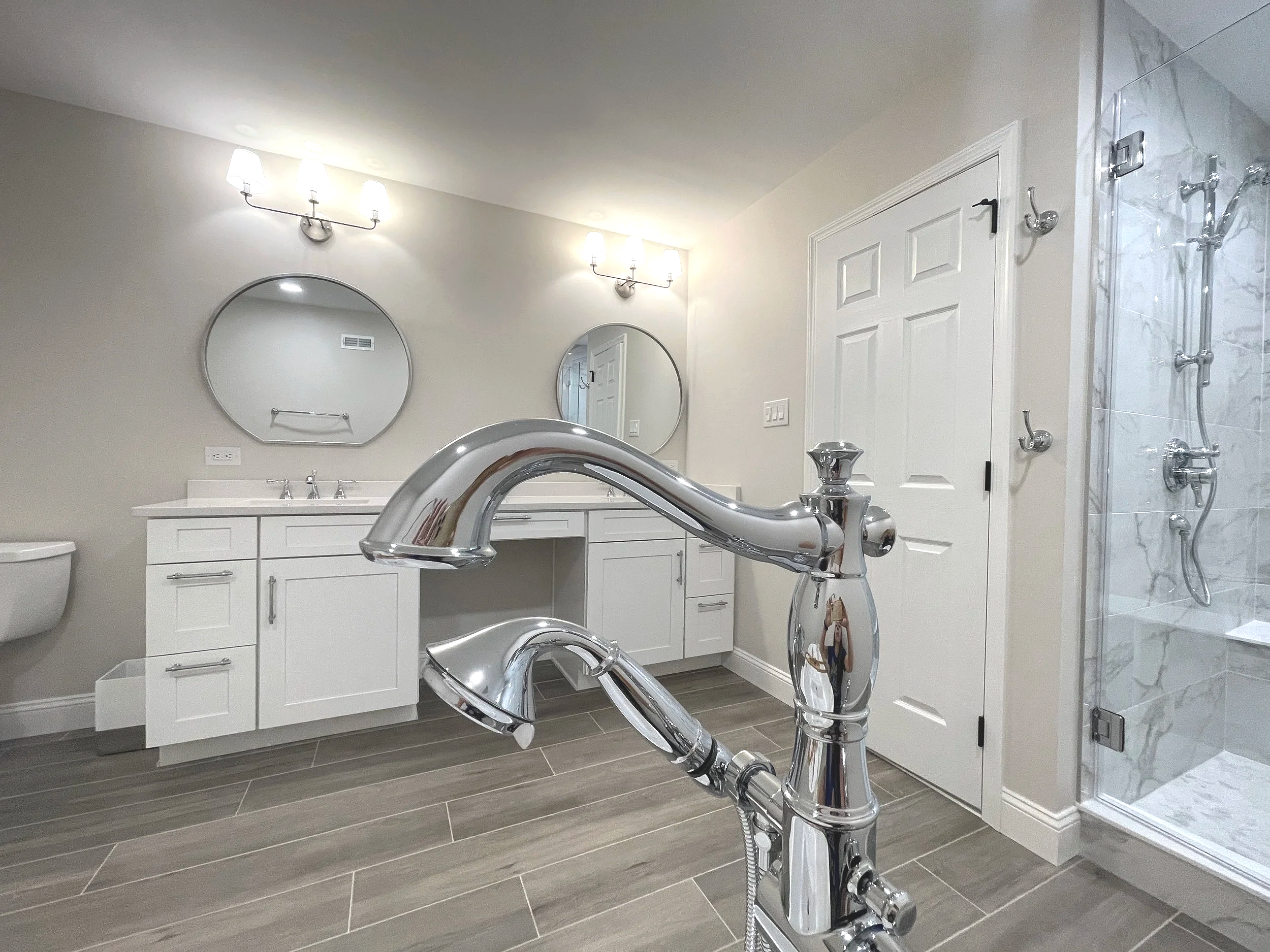 Detail of Delta Cassidy chrome tub filler against a bathroom backdrop of a double vanity with round mirrors, designed and photographed by Sara Trotter / Chroma Maison Design.