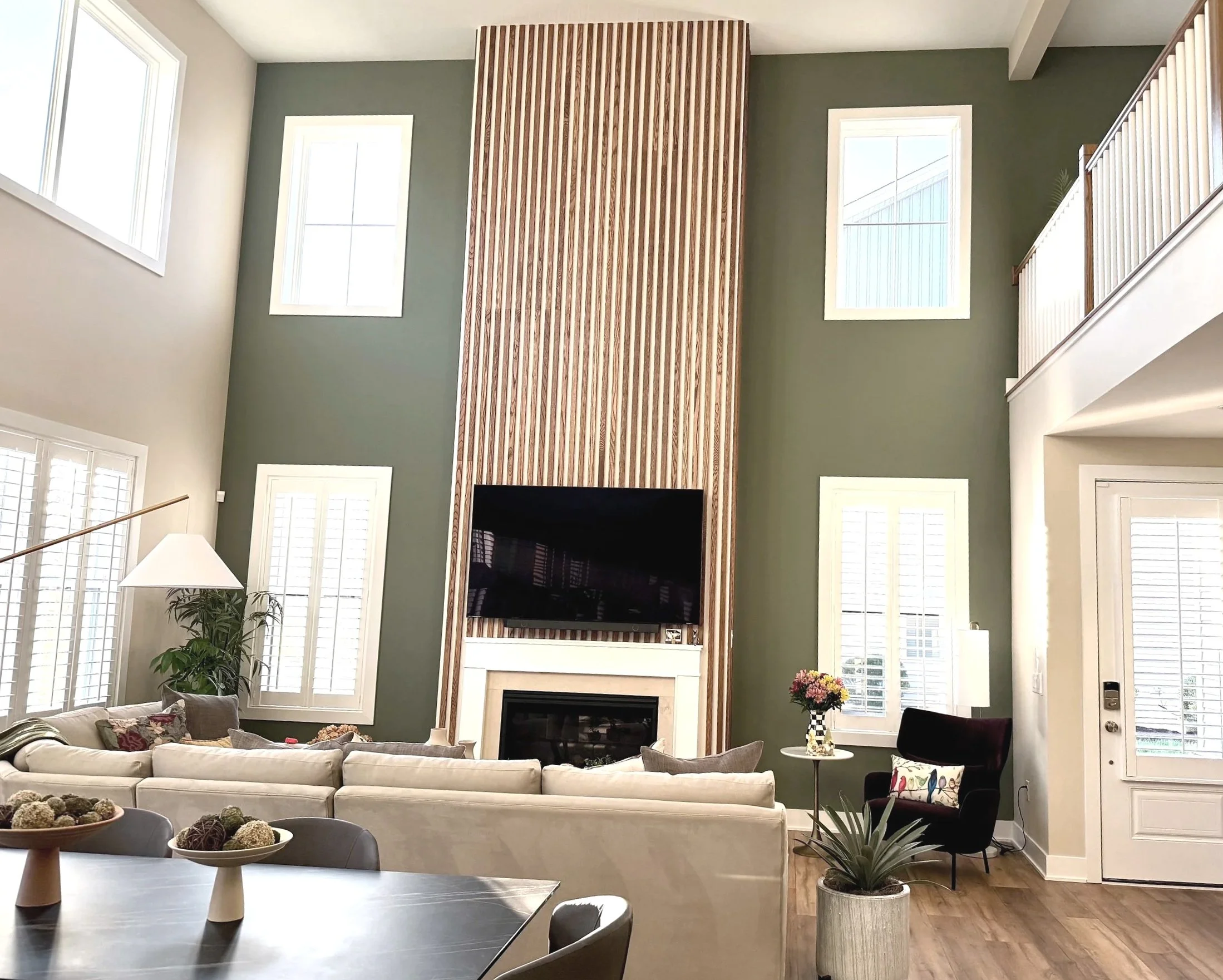 Two story sage green accent wall around a natural wood fluted fireplace. Custom paint plan and photography by Sara Trotter / Chroma Maison Design. 