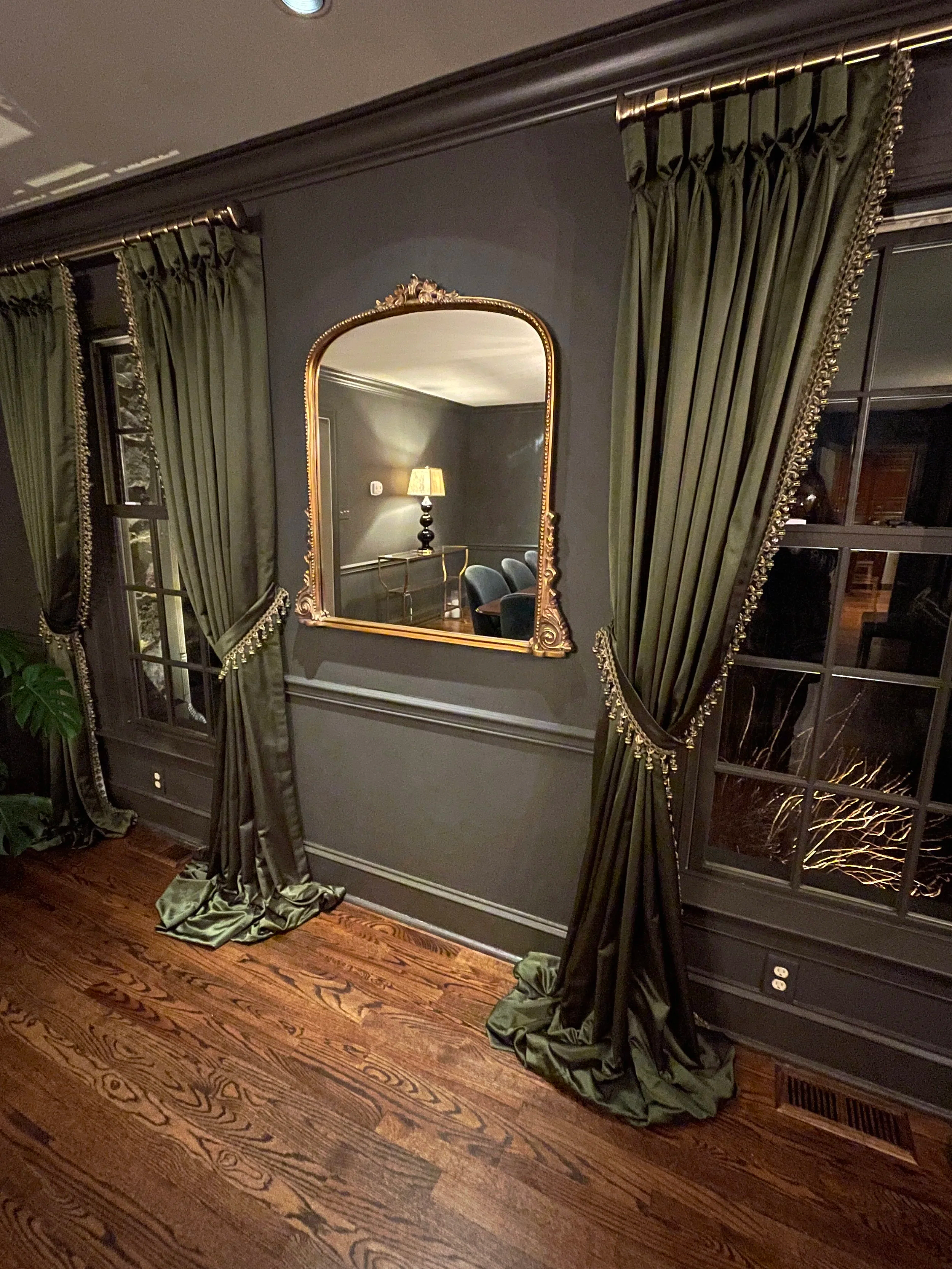 Detail of a brass gilded mirror in a moody color drenched dining room in Urbane Bronze paint.  Featuring rich velvet green floor length curtains.  Custom paint plan and photography by Sara Trotter / Chroma Maison Design.