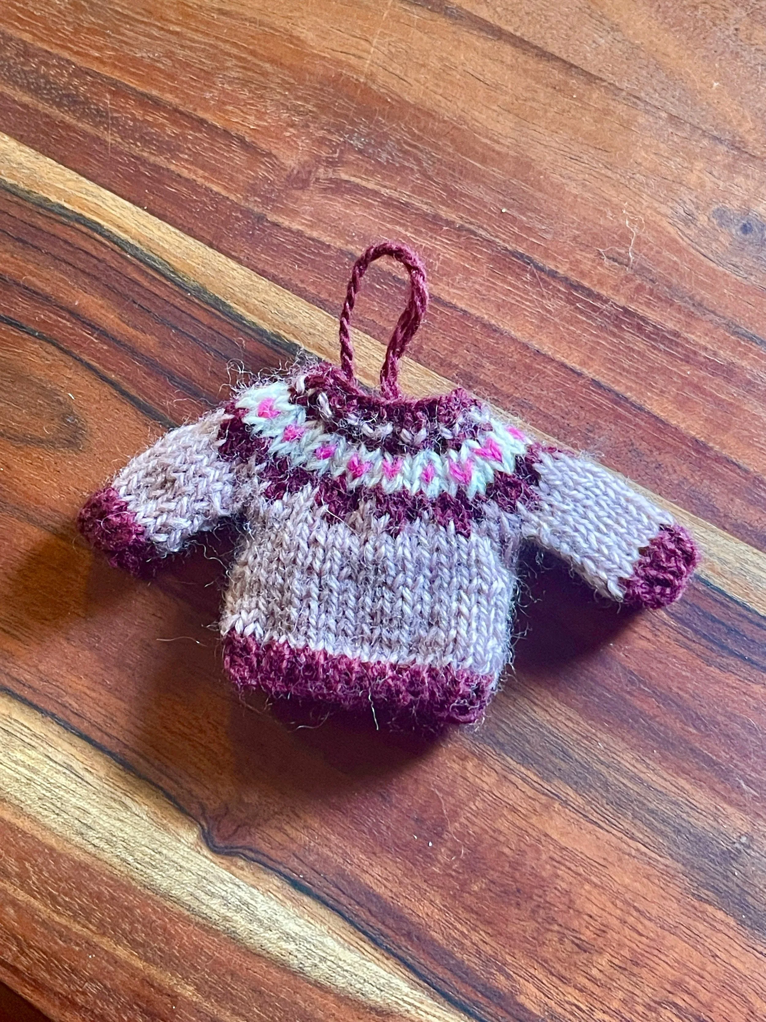 Hand-knit miniature fair isle sweater ornament in pink and maroon colorway, knitted and photographed by artist Sara Trotter.