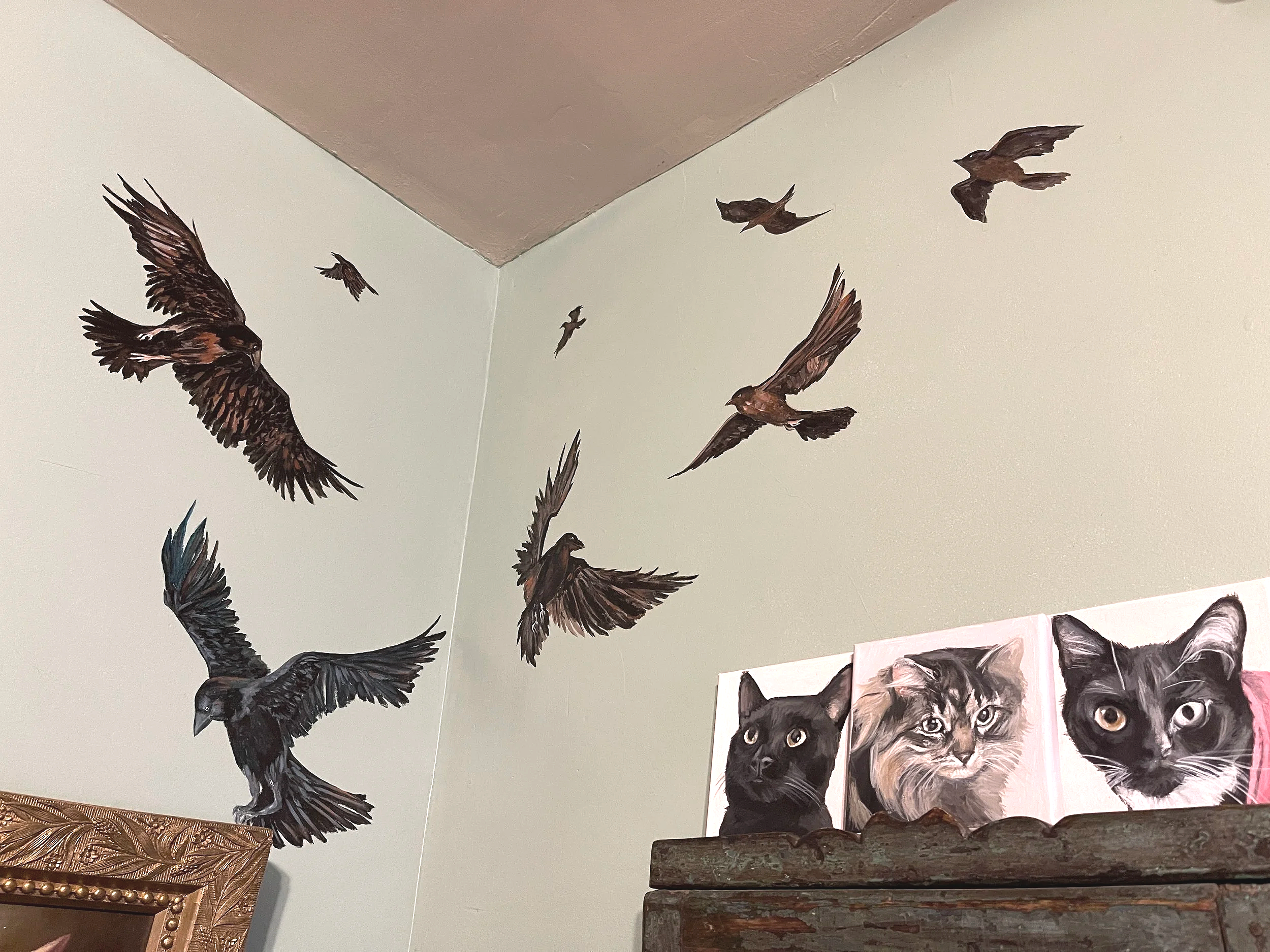 Detail of a hand-painted wall mural featuring a murder of crows swirling in circle in the corner of a room with cats looking up, painted by Sara Trotter / Chroma Maison Design.