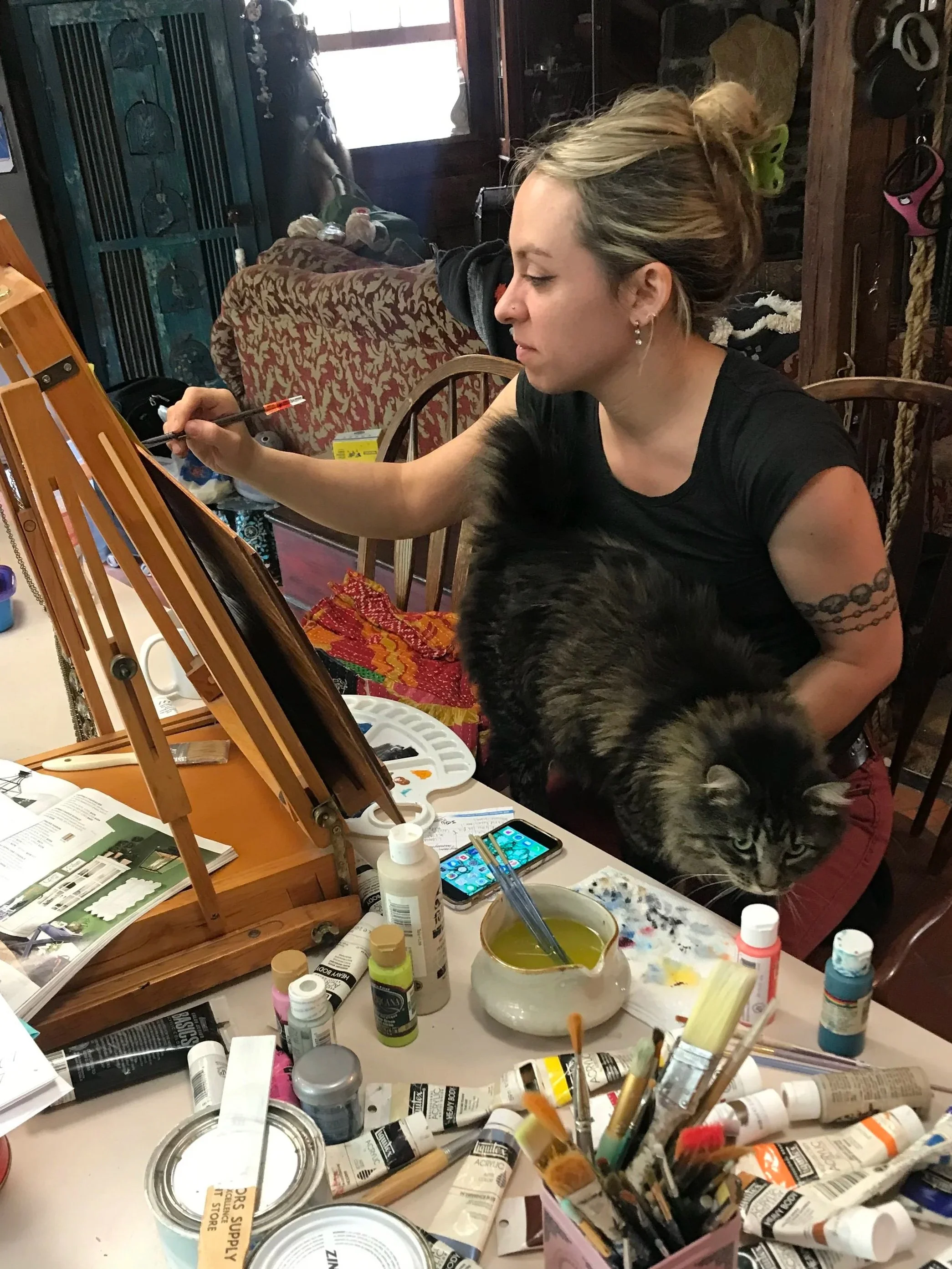 Sara Trotter, an artist, in her barn studio painting with her cat Saucy in her lap, photography by Chroma Maison Design.
