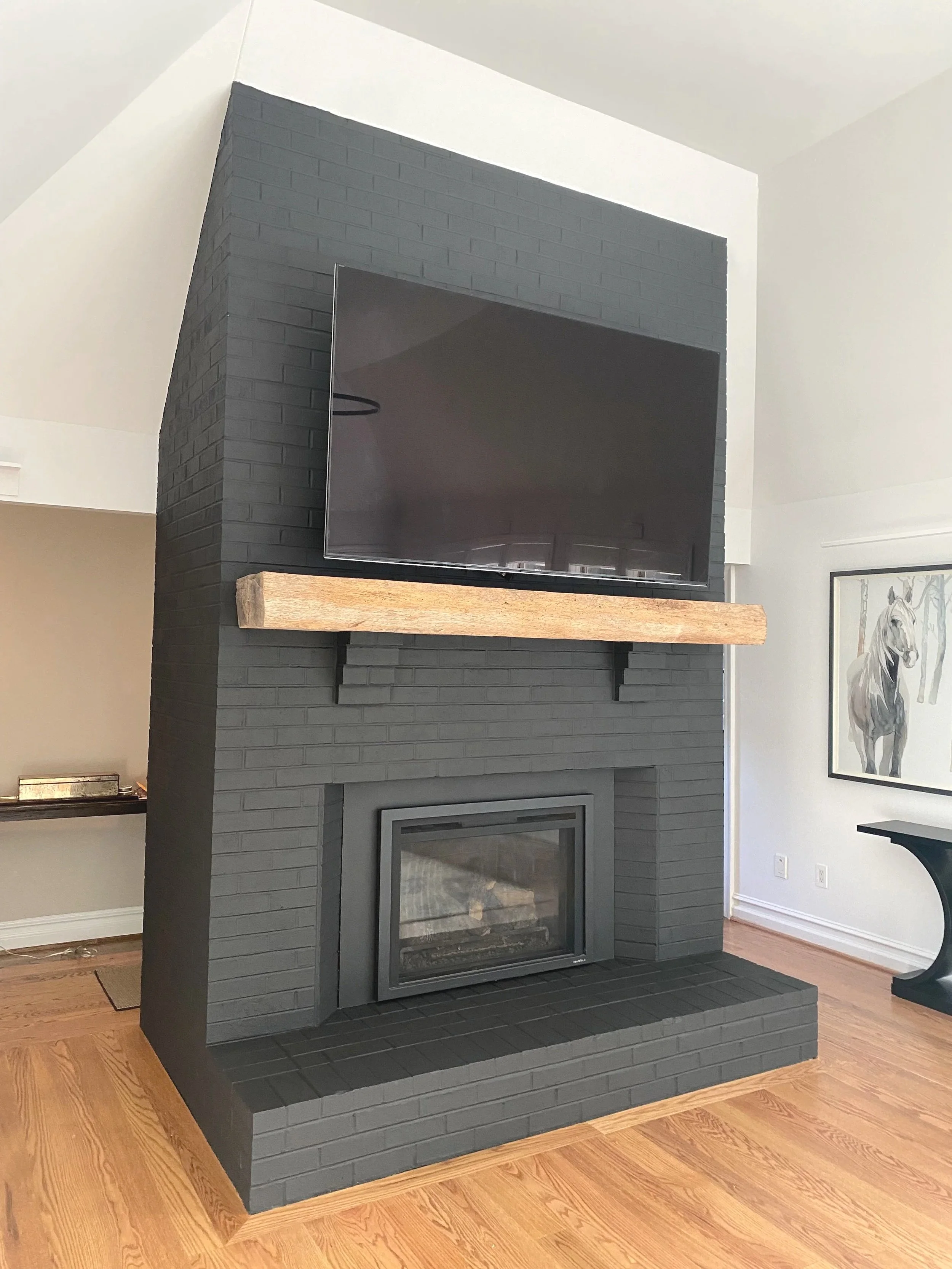 Black matte painted brick fireplace with an oak mantle and hardwood floors.  Custom paint plan by Sara Trotter / Chroma Maison Design.