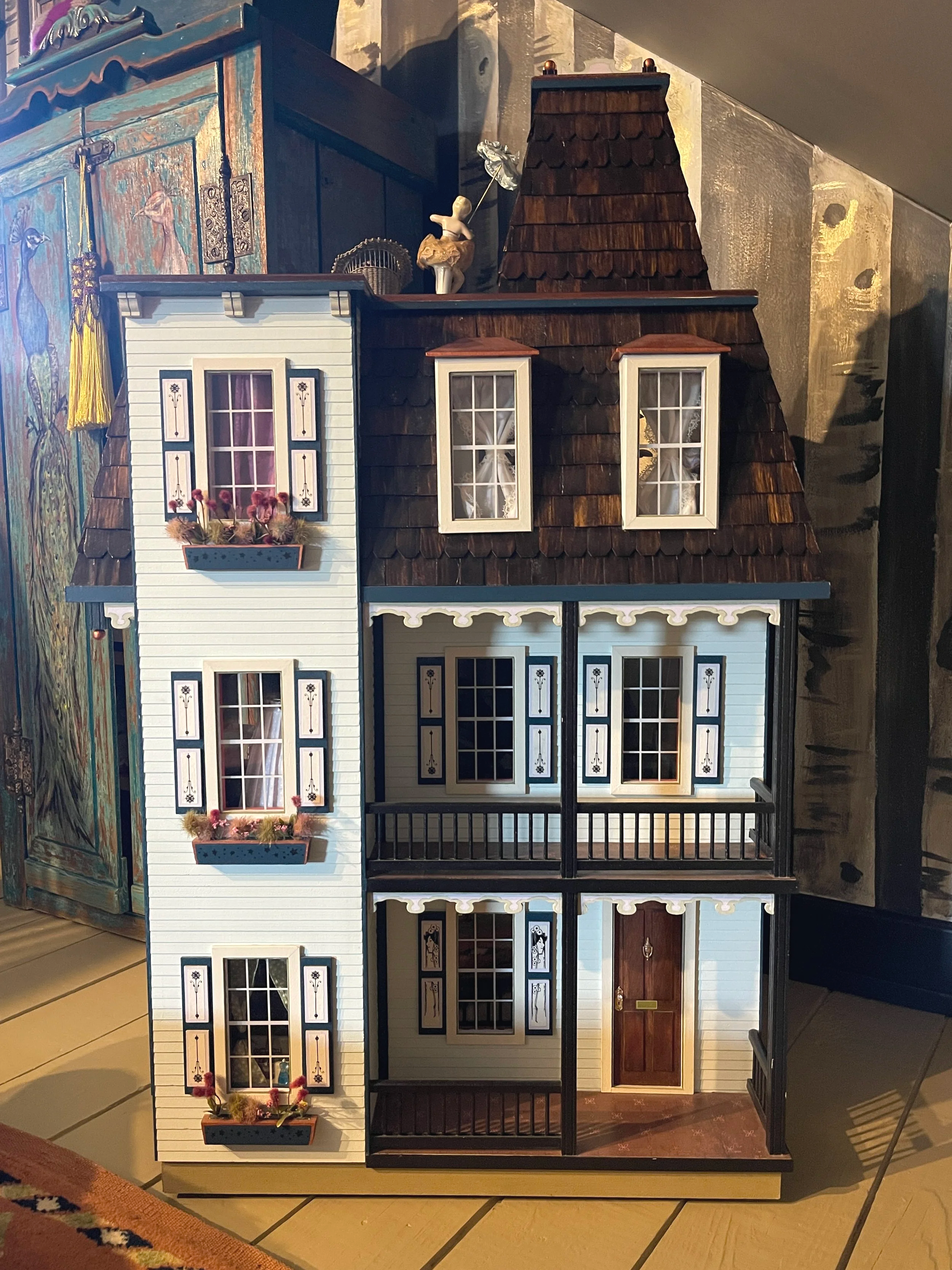 Exterior view of a miniature Victorian dollhouse featuring a cedar shake roof and hand-painted walls, designed by Sara Trotter / Chroma Maison Design.