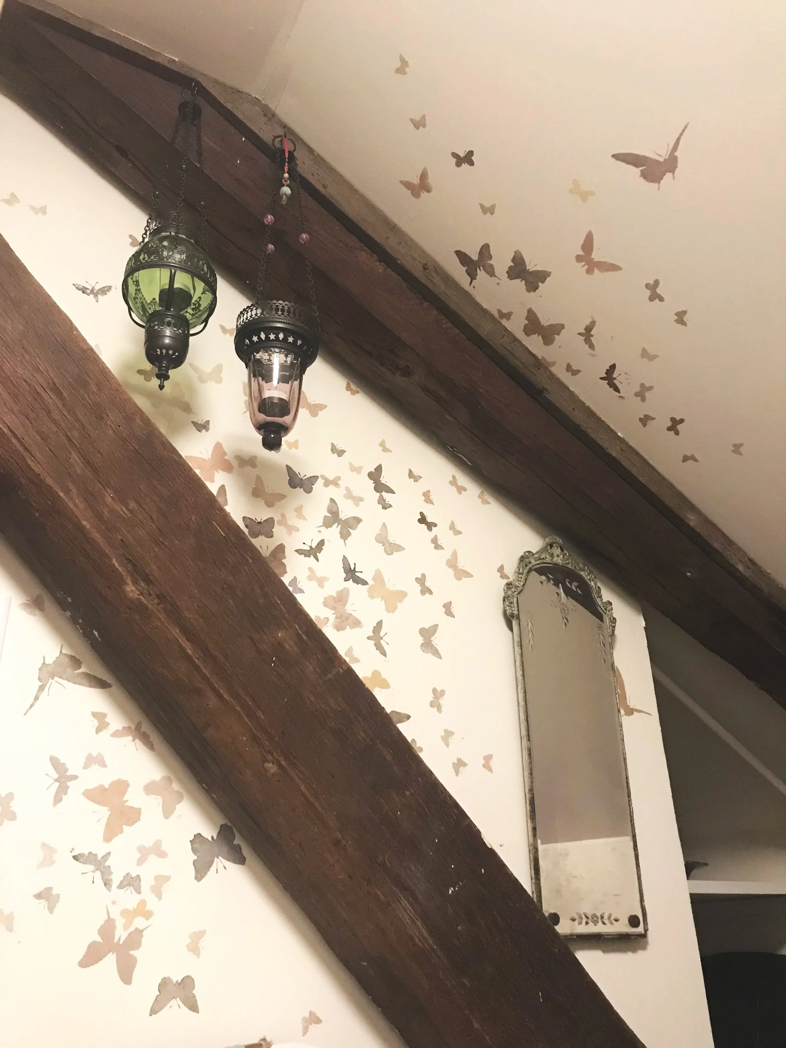 Detail of a hand-painted wall mural with a burst of shimmery moths flying between two historic barn beams, designed and painted by Sara Trotter / Chroma Maison Design.