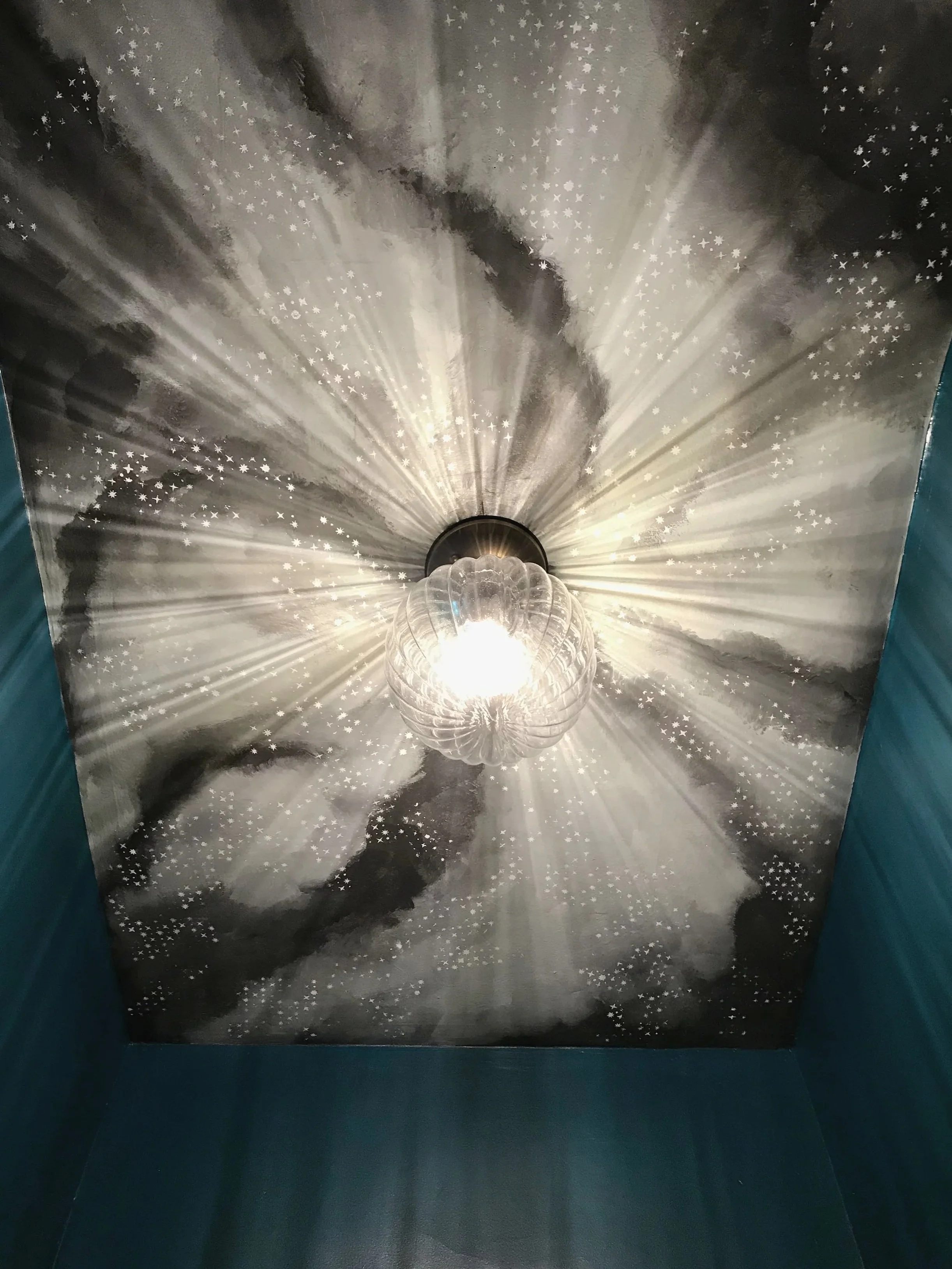 Hallway ceiling painting of a stormy cloudy night sky with tiny stars around a clear ribbed ceiling flush-mount light, painted by Sara Trotter / Chroma Maison Design.