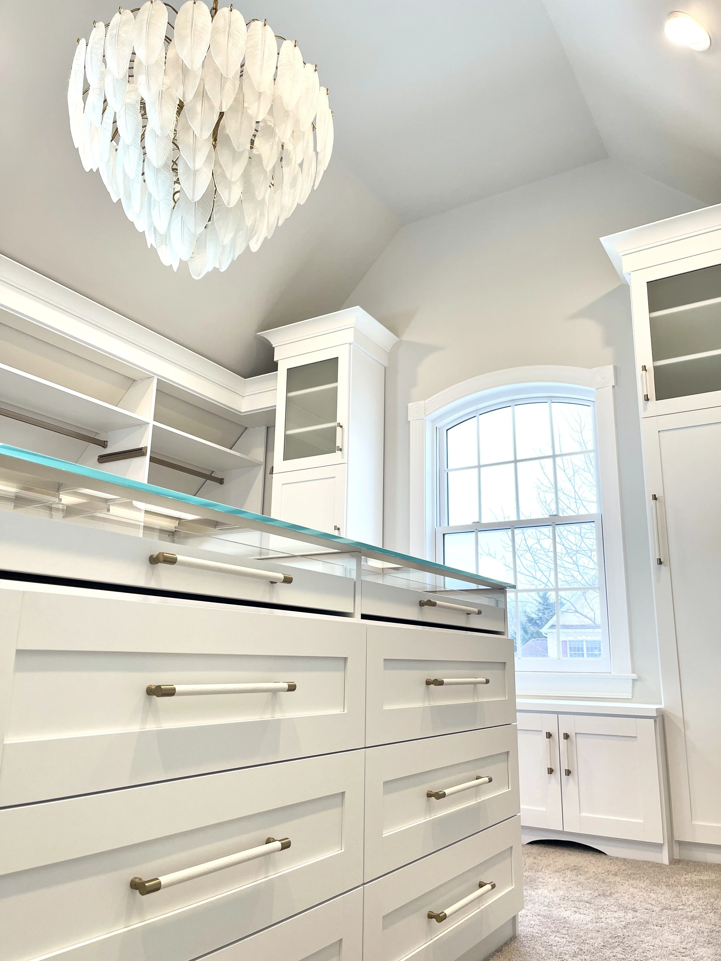 Custom closet with stunning oversized glass feather chandelier above a glass top jewelry island, designed and photographed by Sara Trotter / Chroma Maison Design.