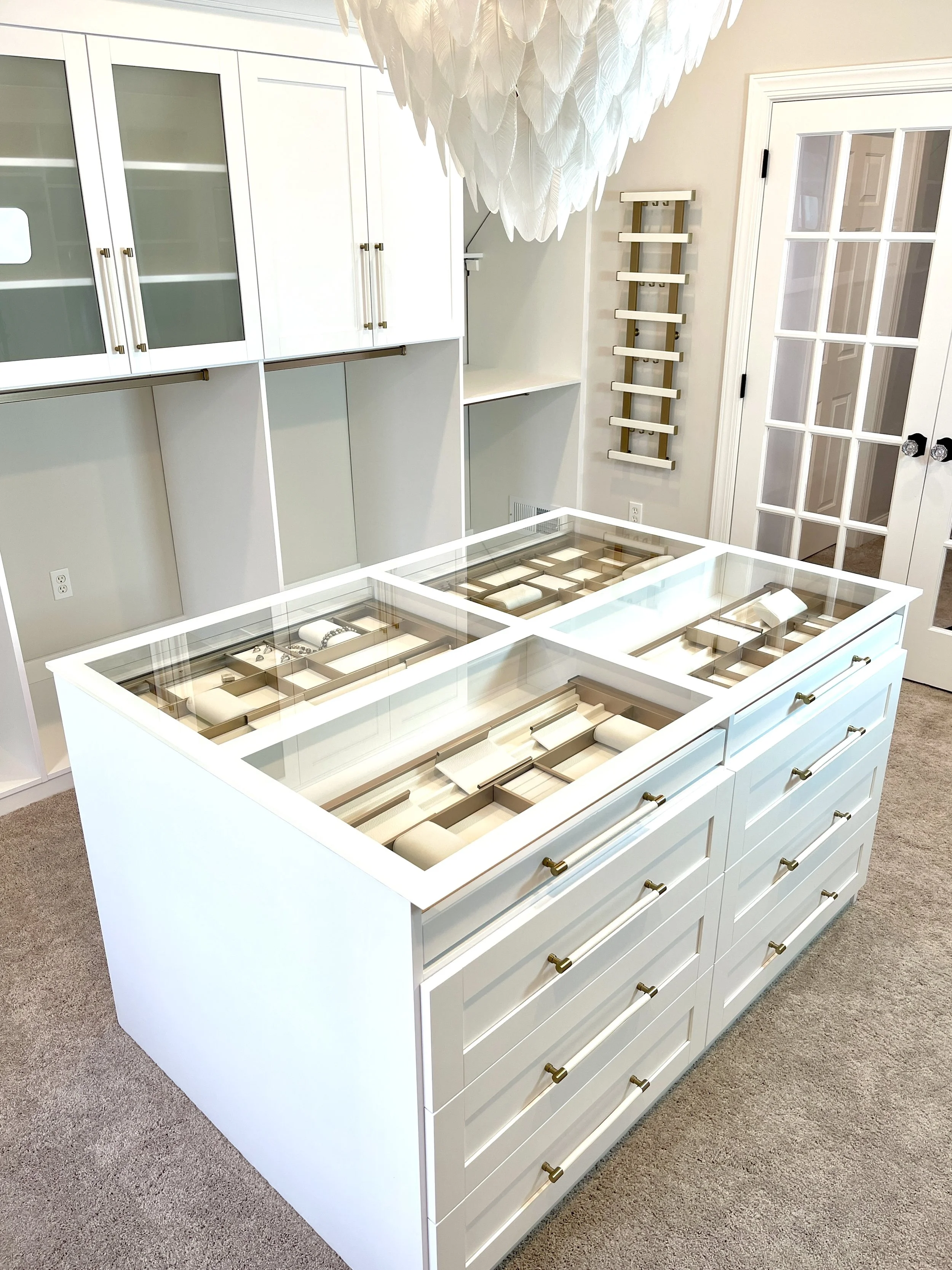 Custom closet with a stunning glass top jewelry island and oversized glass feather chandelier above, designed and photographed by Sara Trotter / Chroma Maison Design.