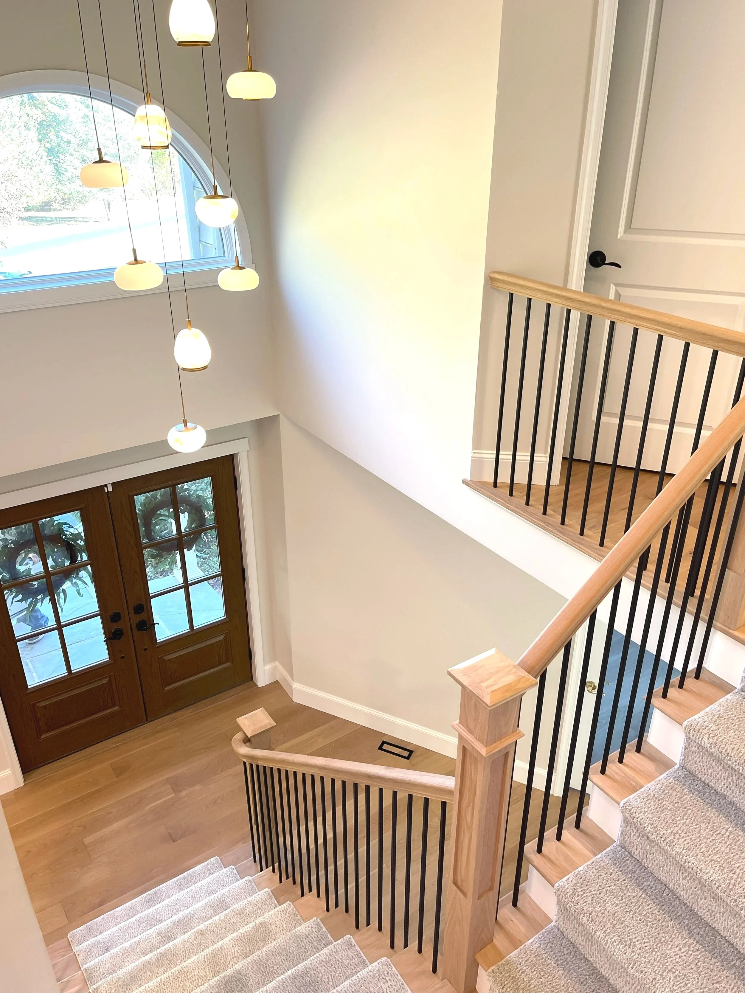 A view from above, on the second floor, looking out over a white oak staircase and the Hinkley light fixture of cascading alabaster pendants in different shapes, designed and photographed by Sara Trotter / Chroma Maison Design.