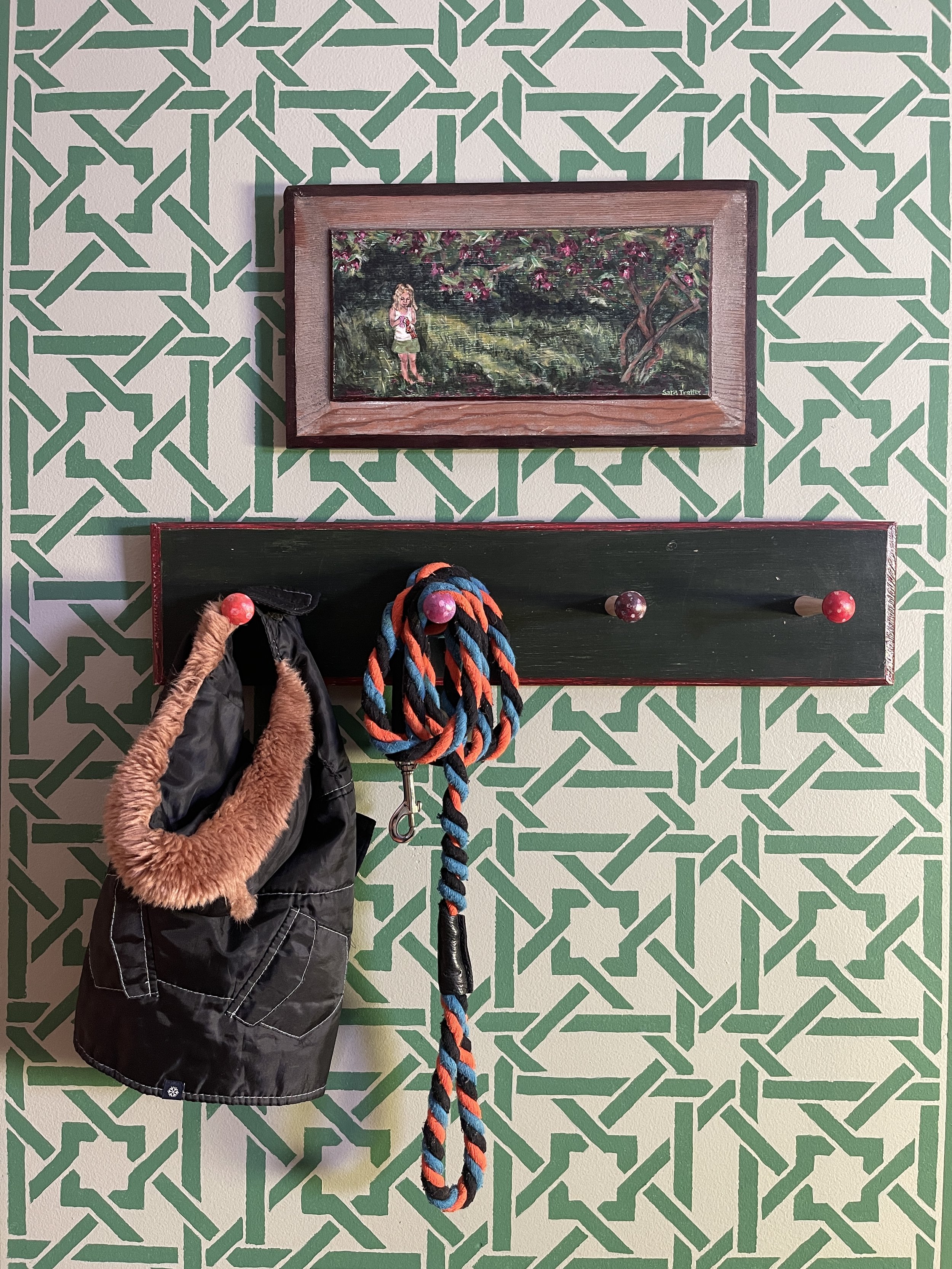 Stenciled green trellis wall with a painting of Camilla Little above a mushroom coat rack with doggie gear, by Sara Trotter.
