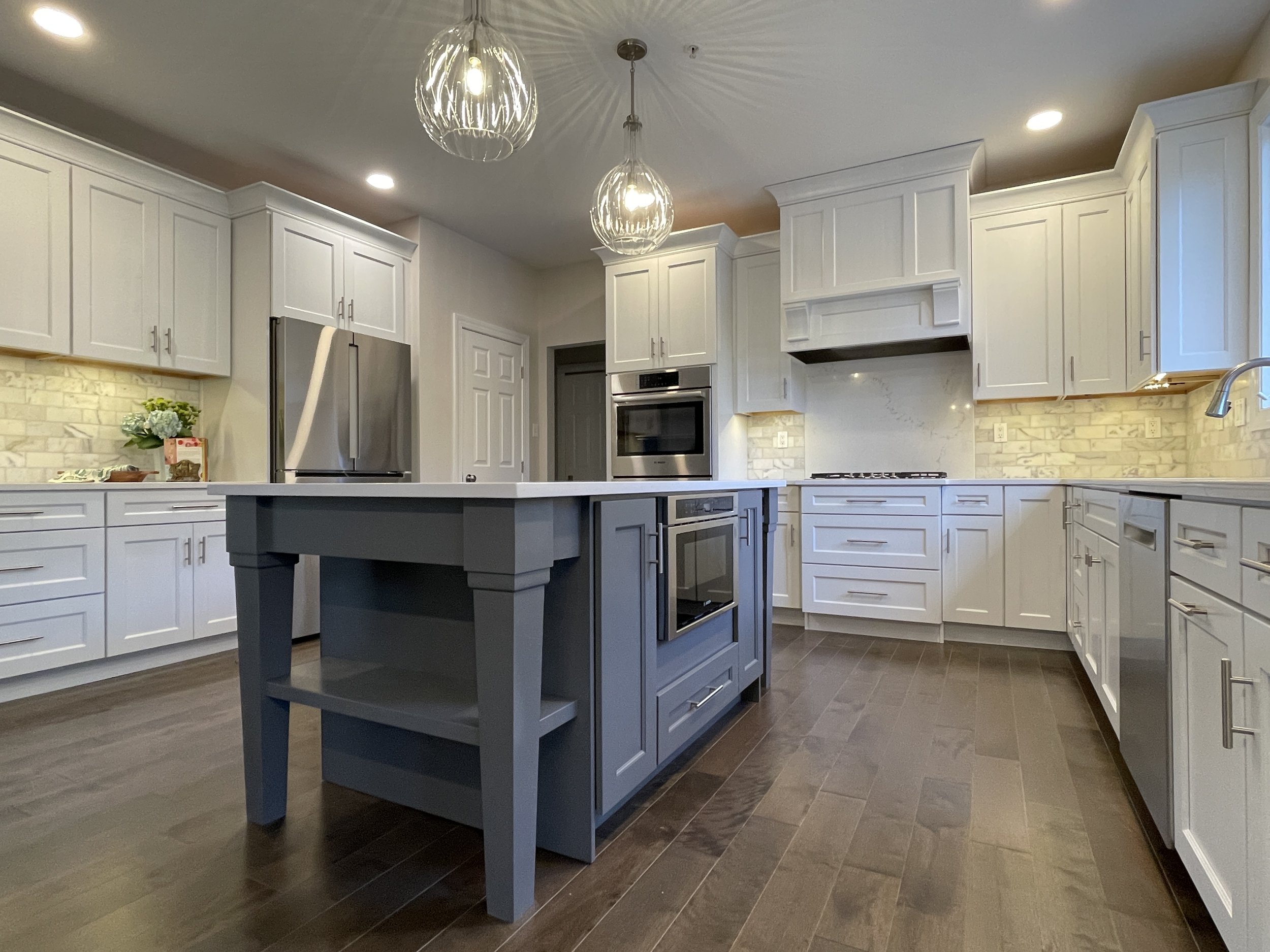 White kitchen with a blue gray vanity showcasing a quartz slab behind the stove and two clear ribbed glass pendants above, designed and photographed by Sara Trotter / Chroma Maison Design.