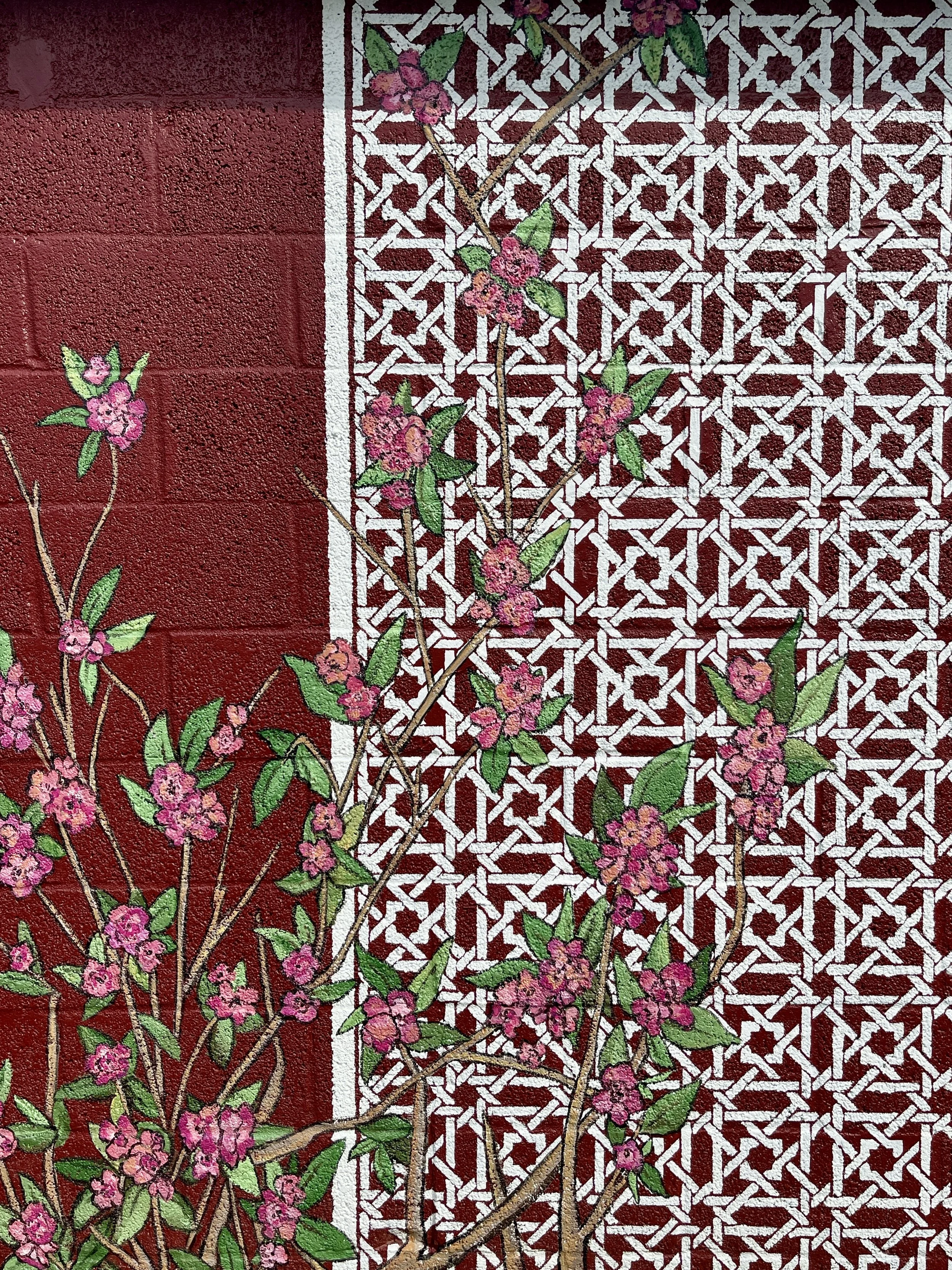 Detail of a hand-painted exterior mural of roses growing over a white trellis on a barn red background, designed and painted by Sara Trotter / Chroma Maison Design.