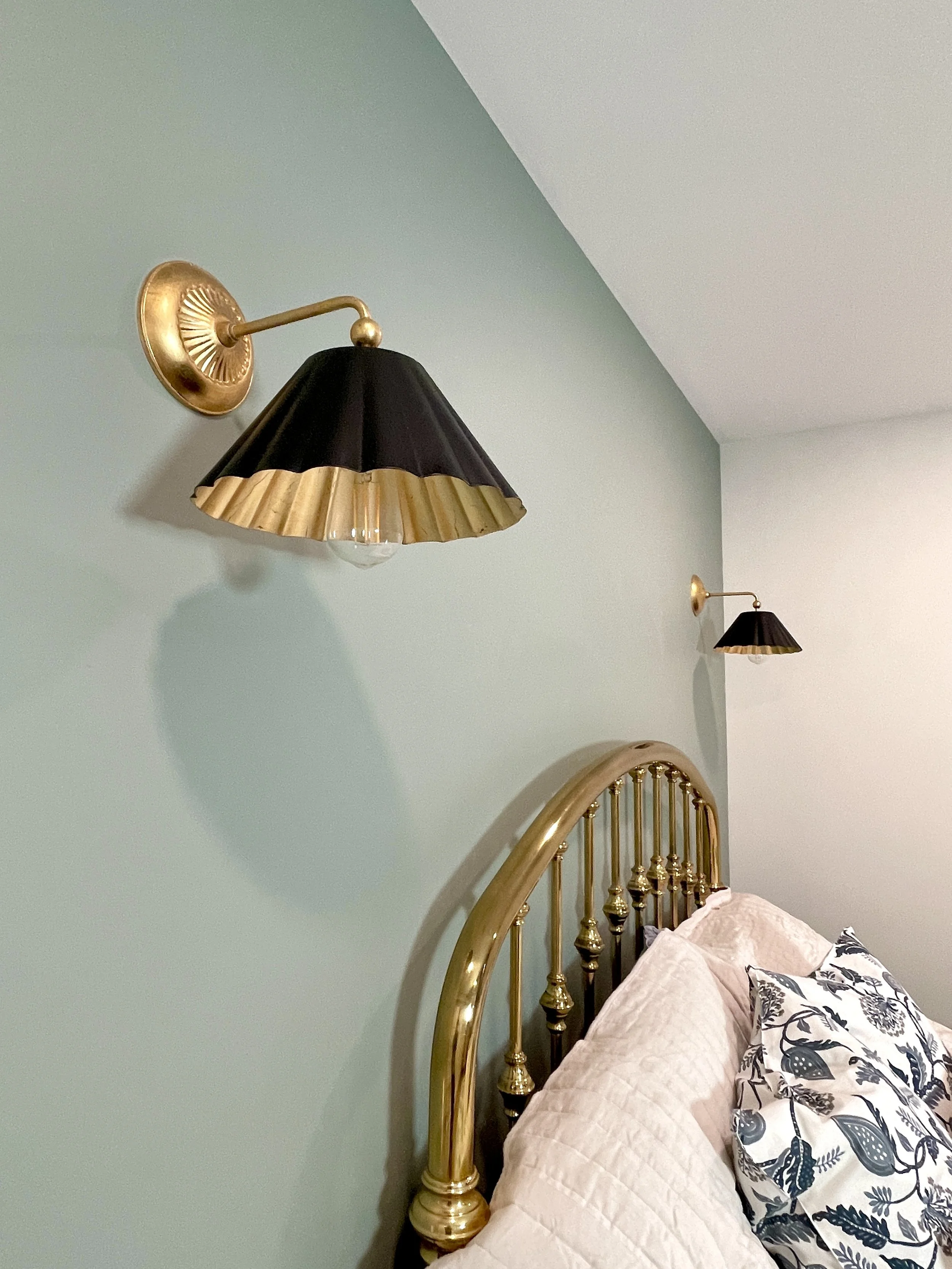 Guest bedroom with an antique brass headboard framed by two black and brass scalloped metal French inspired sconces, designed and photographed by Sara Trotter / Chroma Maison Design.
