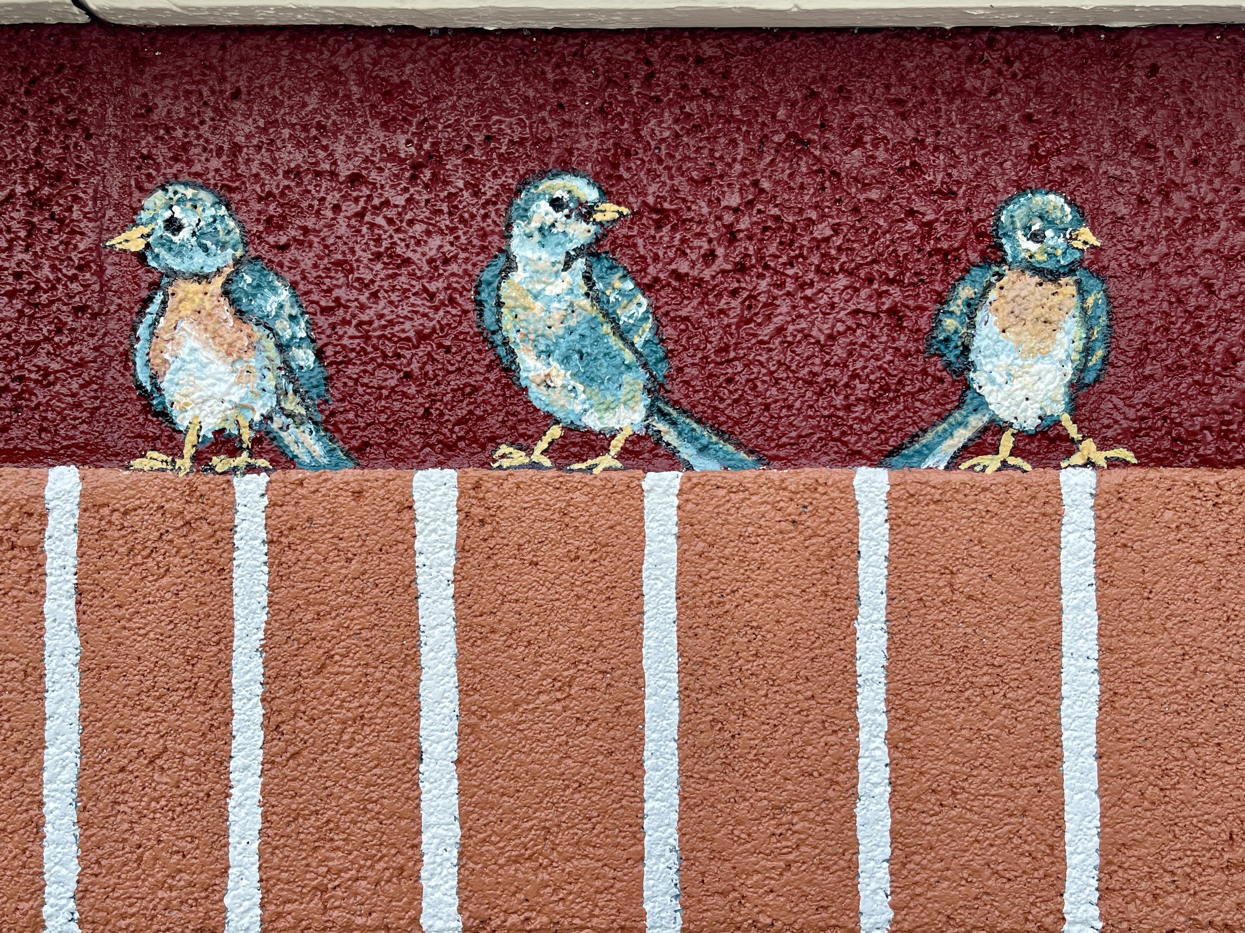 Detail of an exterior hand-painted mural of three bluebirds sitting on faux brick, by artist Sara Trotter / Chroma Maison Design.