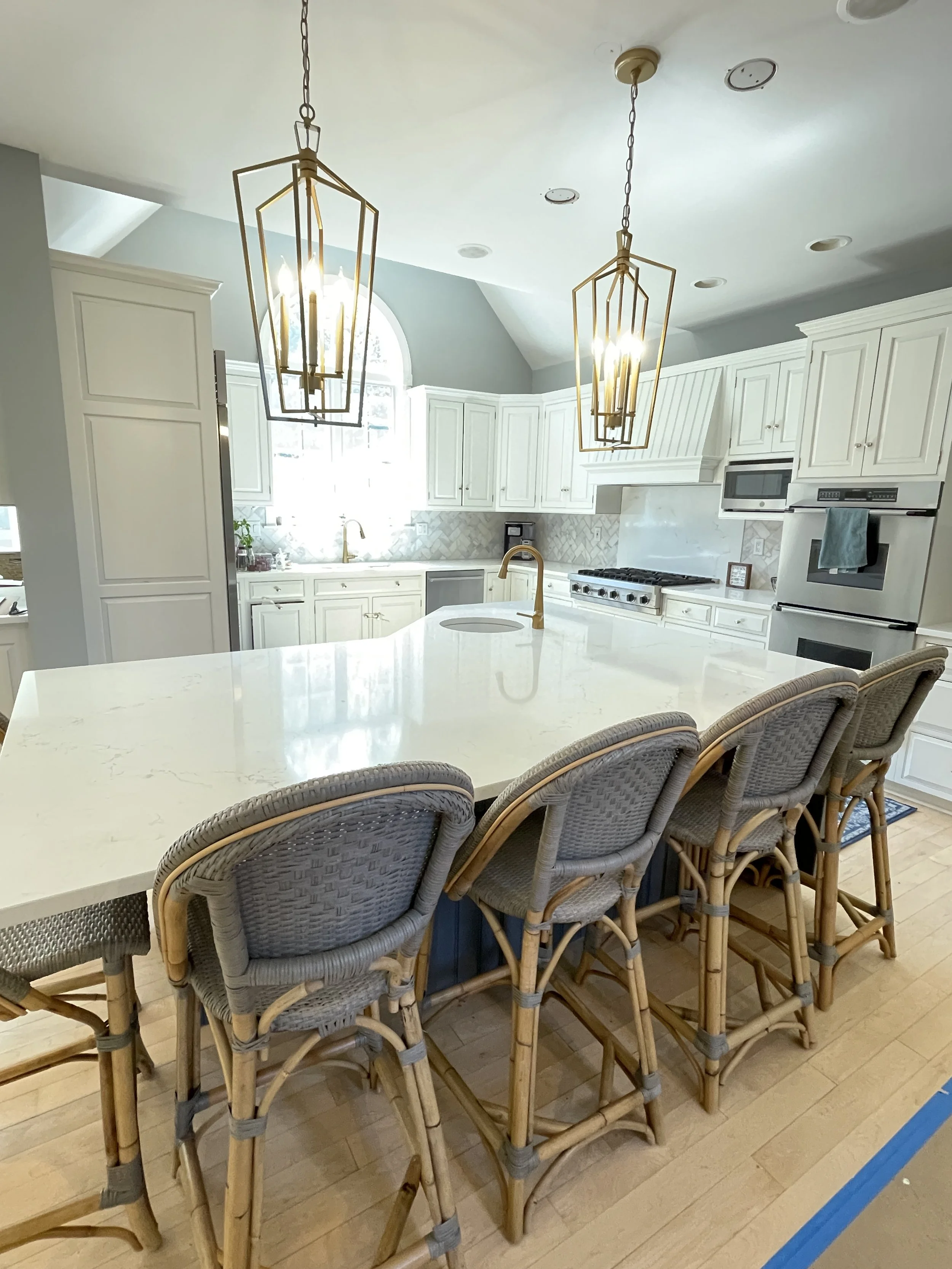 Two over-sized brass birdcage lights above a kitchen island surrounded by gray Serena and Lily rattan chairs, designed and photographed by Sara Trotter / Chroma Maison Design.